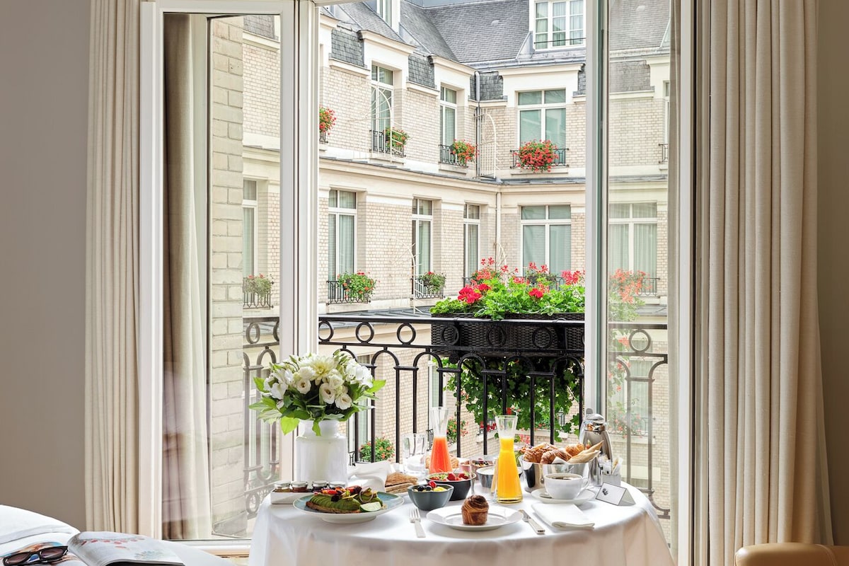 A balcony with a table set for breakfast, overlooking a residential area with balconies and flower boxes.