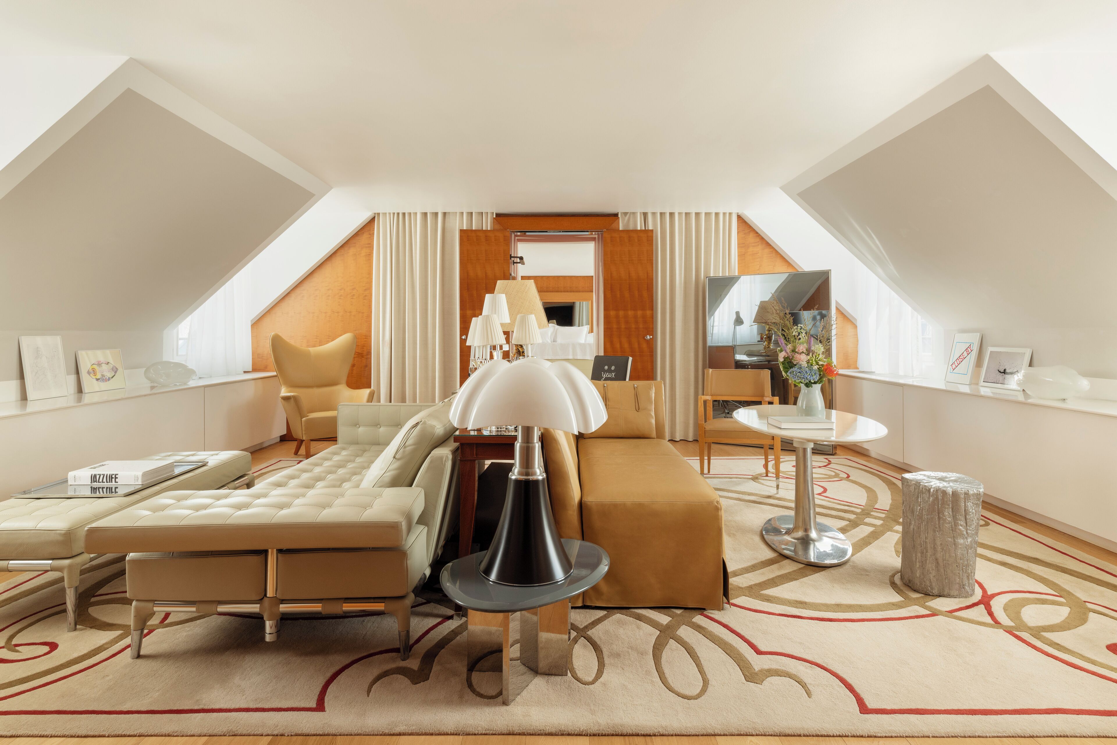 A modern hotel room with a loft design, featuring a large bed, a sitting area, a small table, and a view of the city.