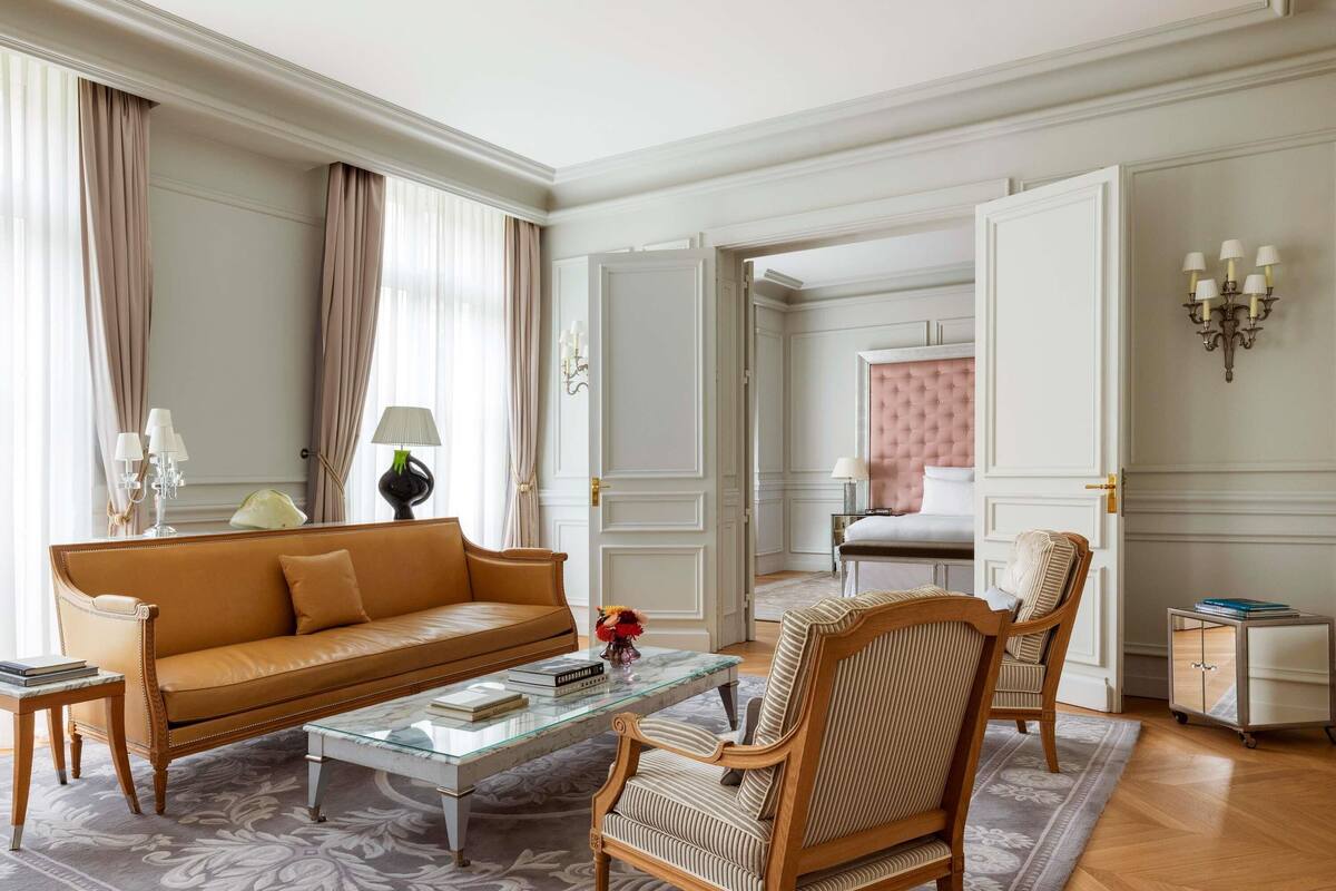 Una sala de estar elegantemente decorada con un sofá de cuero, una mesa de centro de vidrio, un tapiz estampado y una silla de madera clásica.