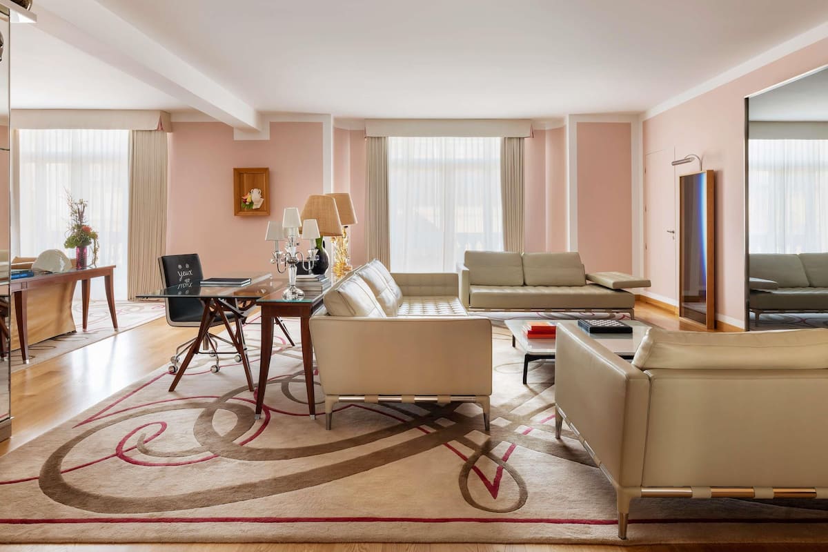 A modern hotel room with a dining area, a sofa, a coffee table, and a TV.
