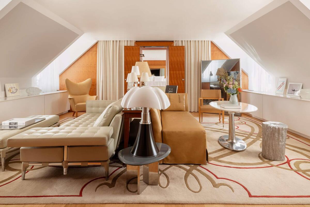 A modern hotel room with a loft design, featuring a sofa, a small round table, a lamp, and a mirror.