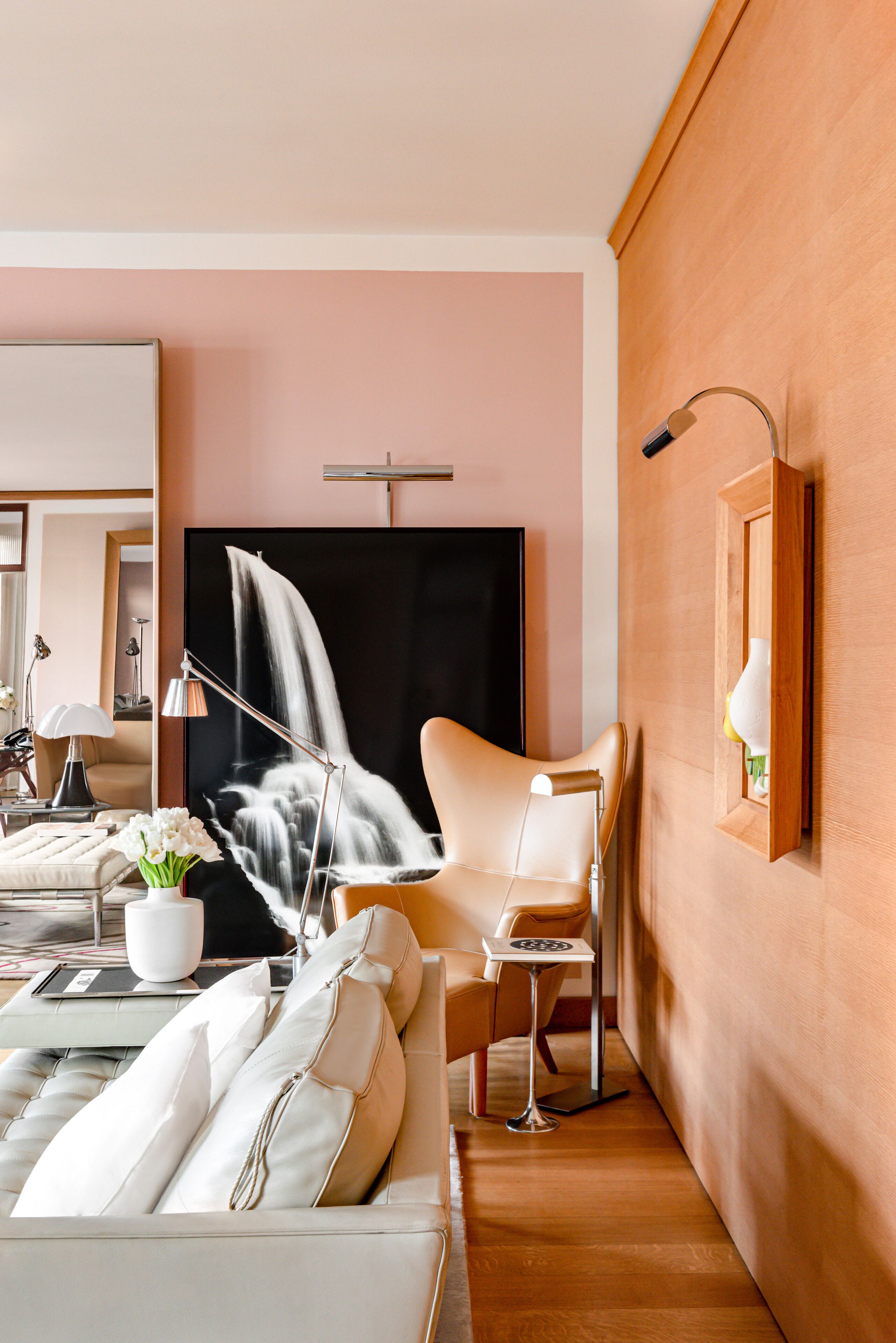 Una habitación de hotel moderna con un televisor de pantalla plana grande, un sofá con cojines blancos, una mesita auxiliar pequeña y un jarrón decorativo con flores.