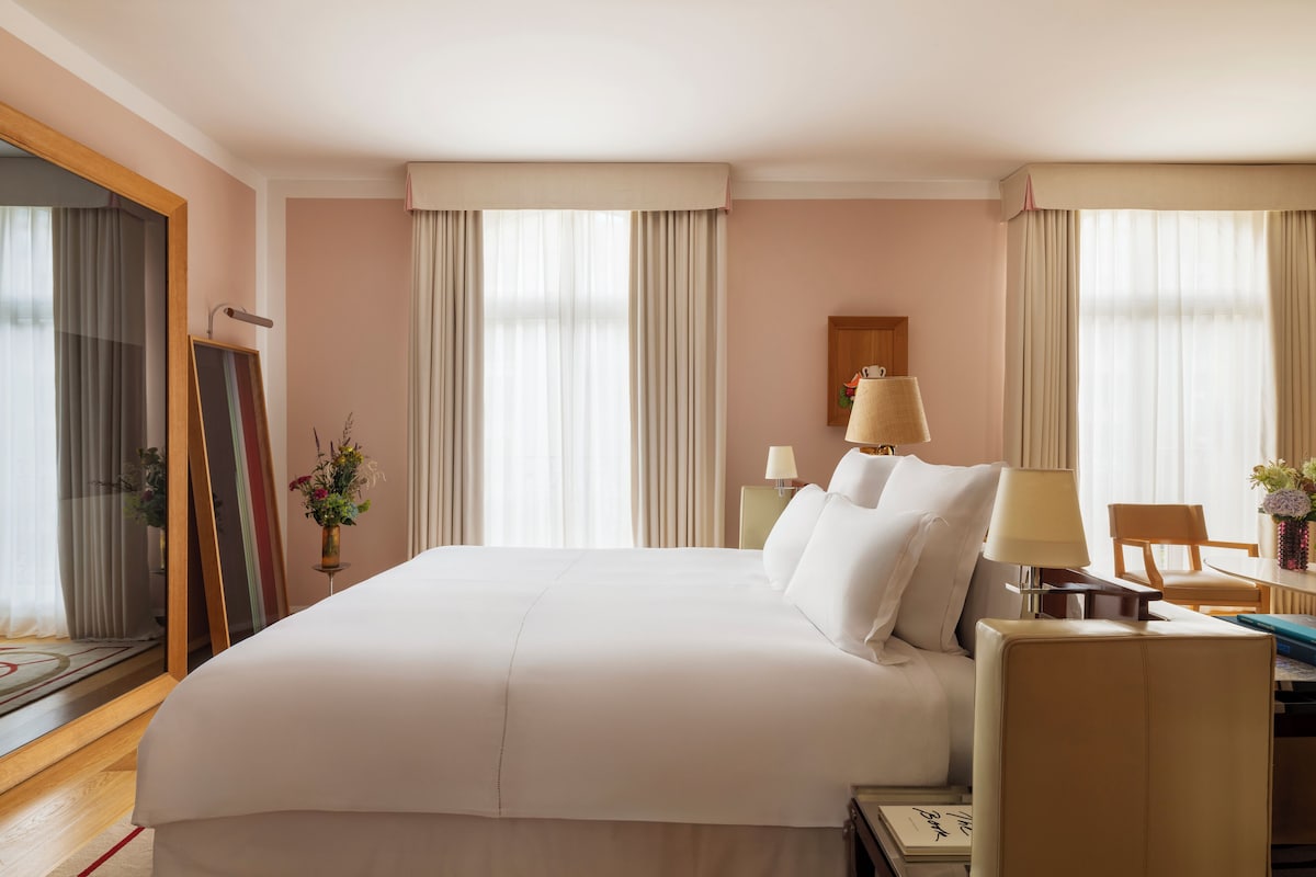 A hotel room with a large bed, a desk with a chair, a lamp, and a mirror.