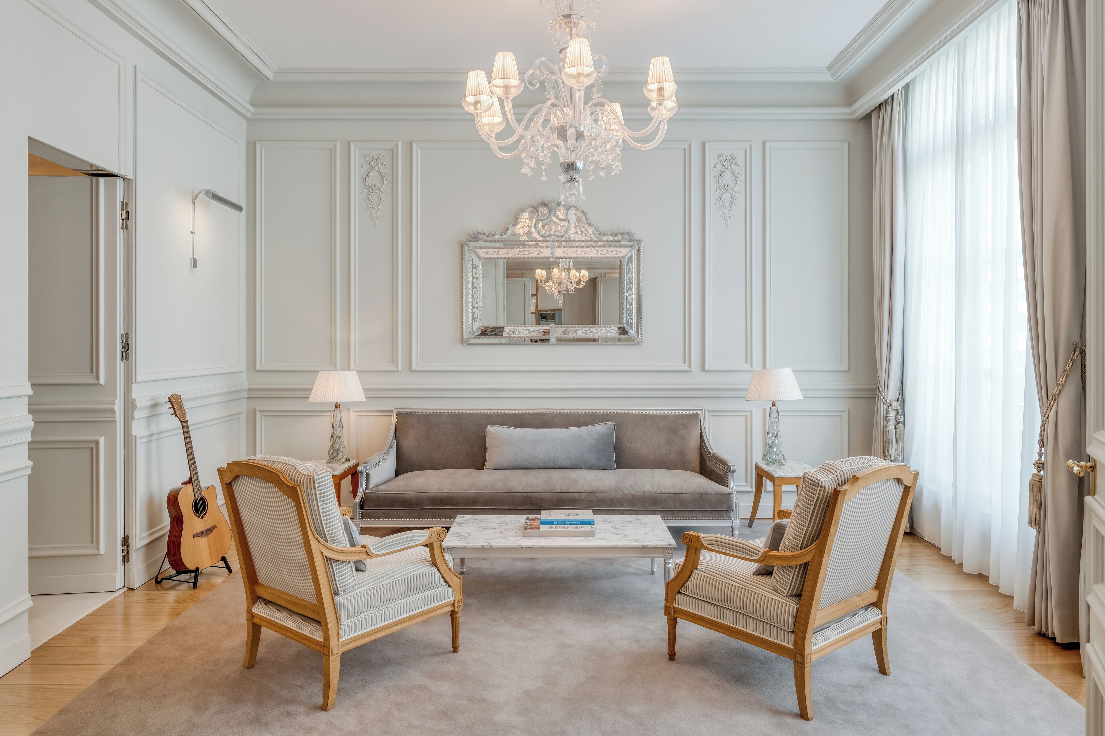 A spacious living room with a large sofa, two armchairs, a coffee table, a chandelier, and a mirror on the wall.