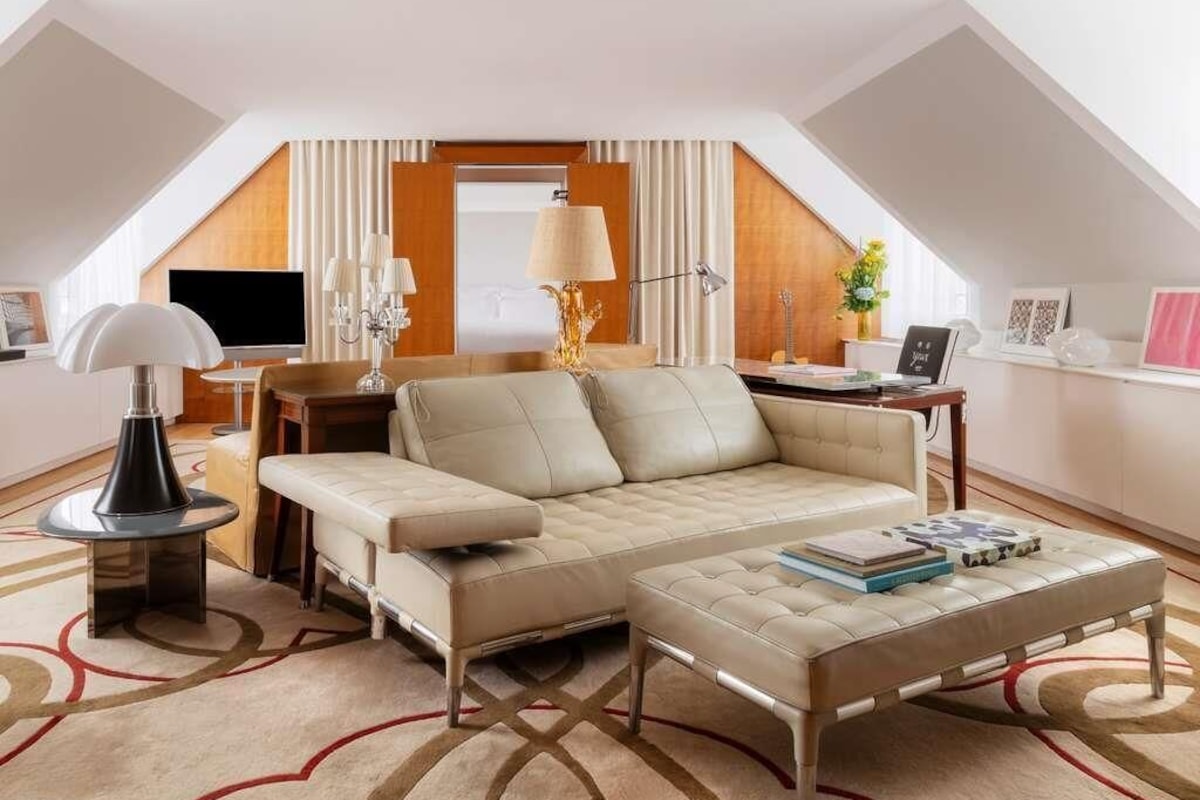 A modern loft-style room with a sofa, ottoman, and a flat-screen TV.