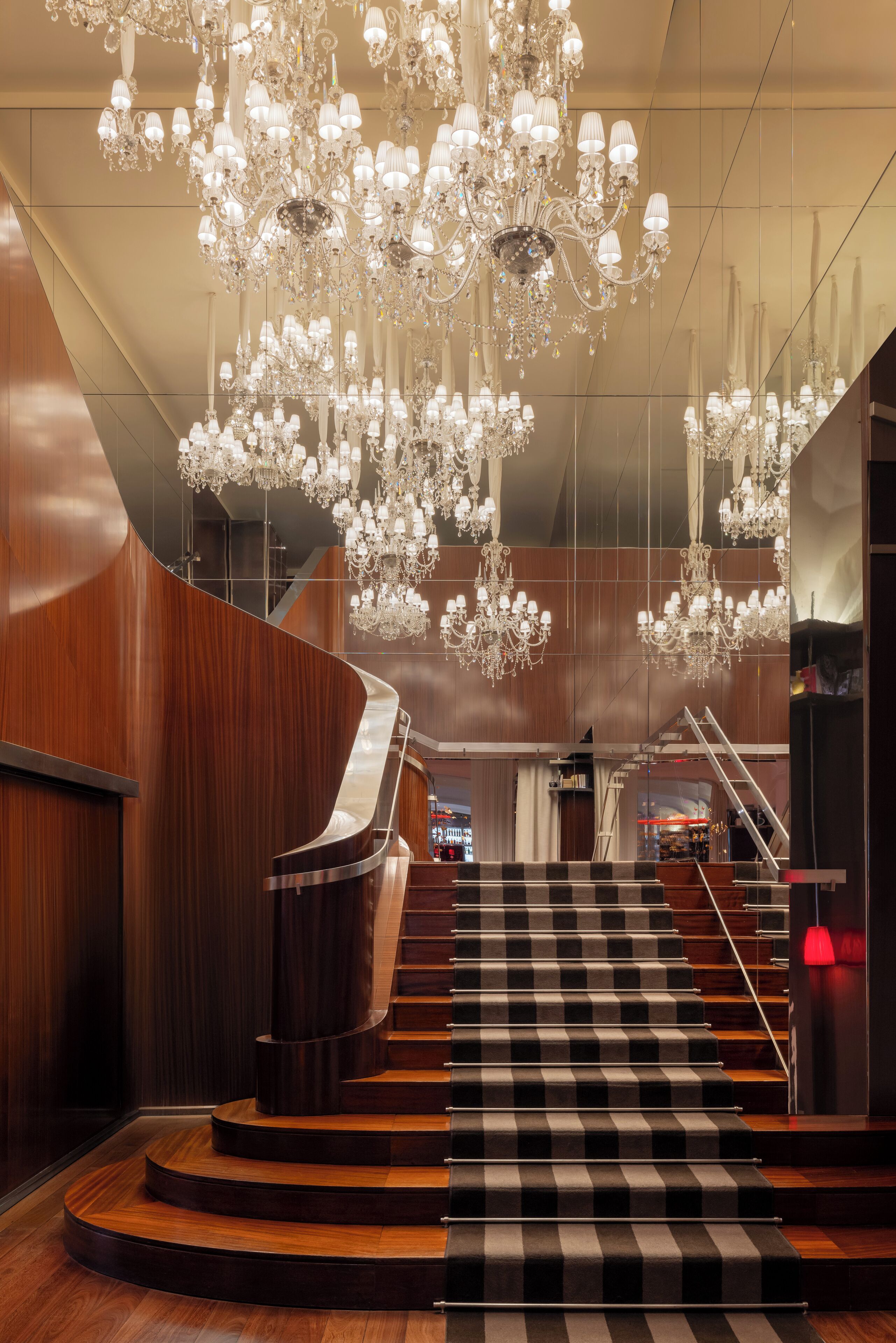 A grand staircase with a black and white checkered carpet, surrounded by wooden paneling and multiple chandeliers.