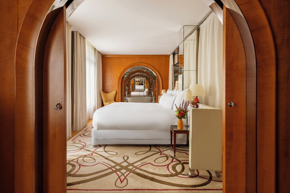 A hotel room with a large bed, a nightstand with a lamp, and a mirror.