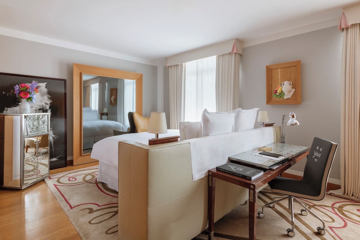 A hotel room with a bed, desk, chair, and a mirror.