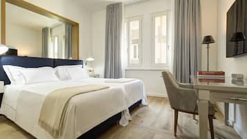Habitación de hotel con una cama grande, un escritorio y una silla. Hay un espejo en la pared, una lámpara en el escritorio y cortinas en las ventanas.