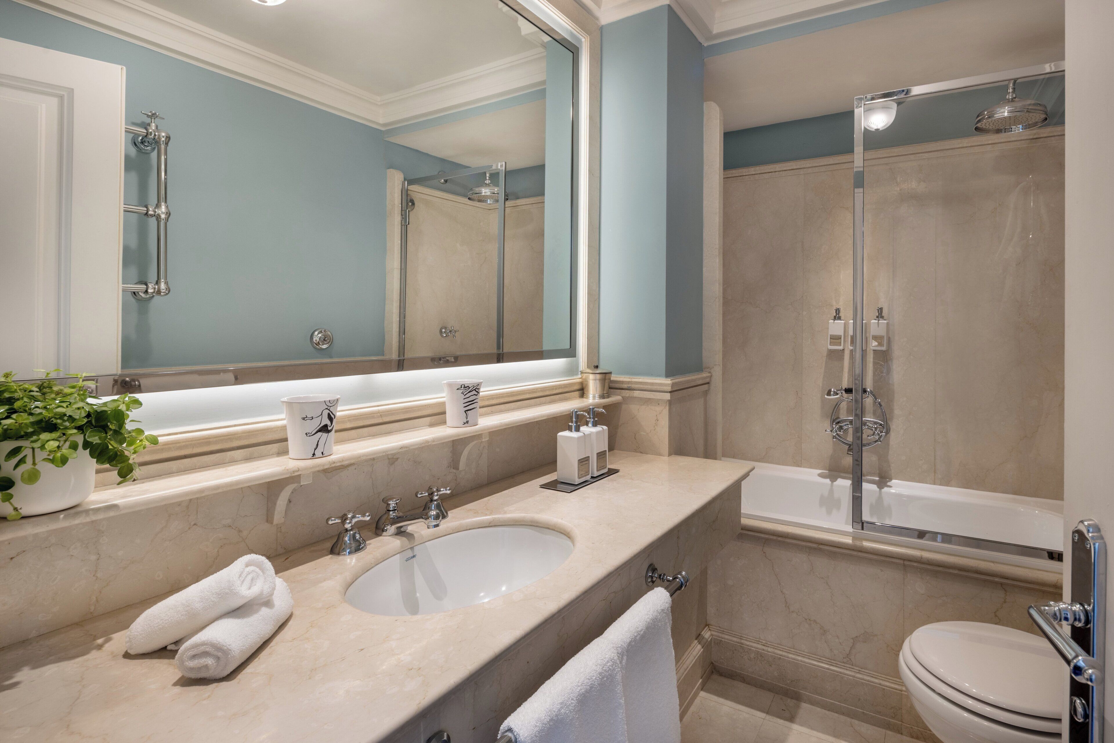 A modern bathroom with a double sink, a large mirror, a glass-enclosed shower, and a toilet.