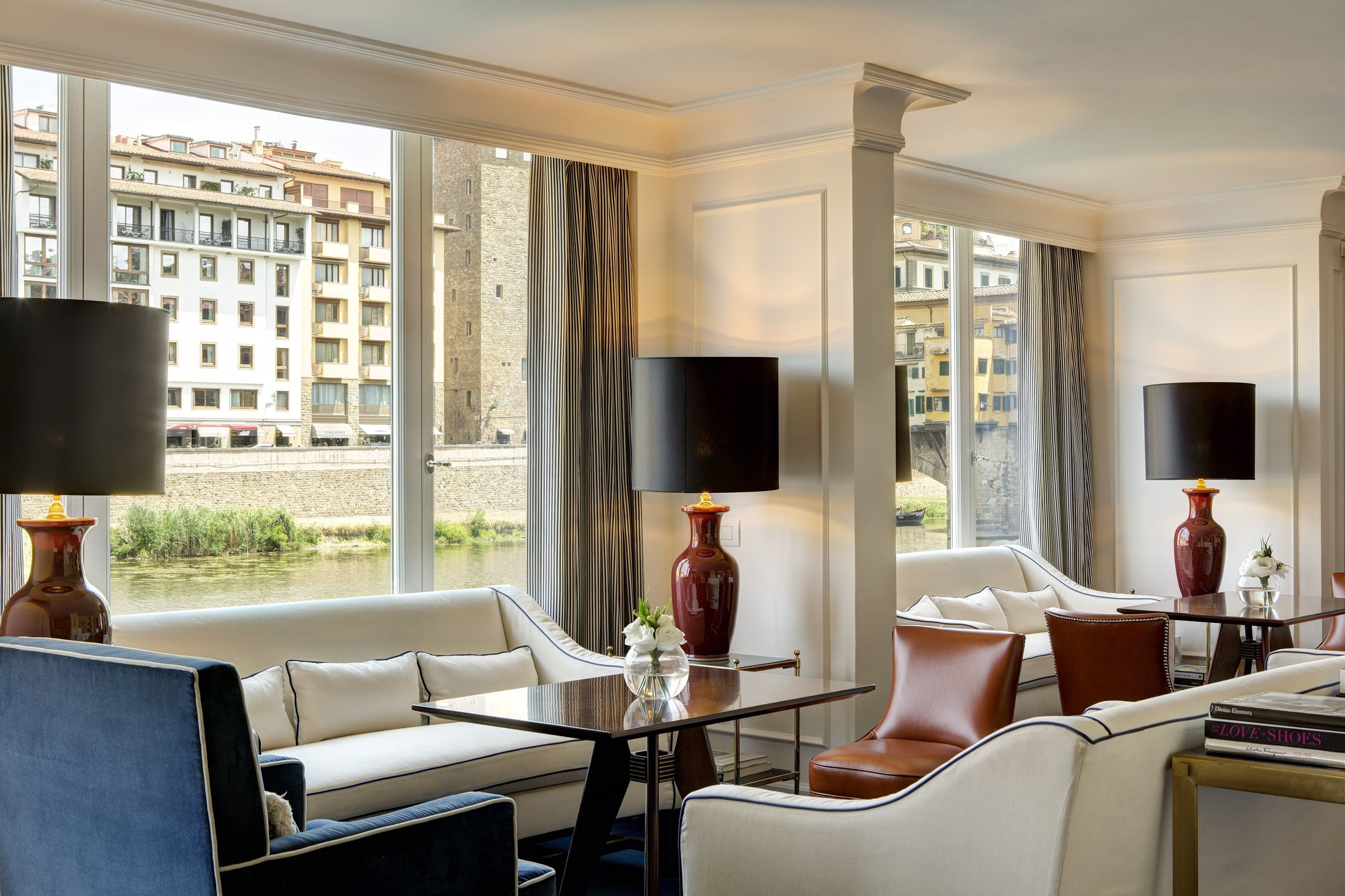 A hotel room with a large window, a sofa, a table, and two lamps.