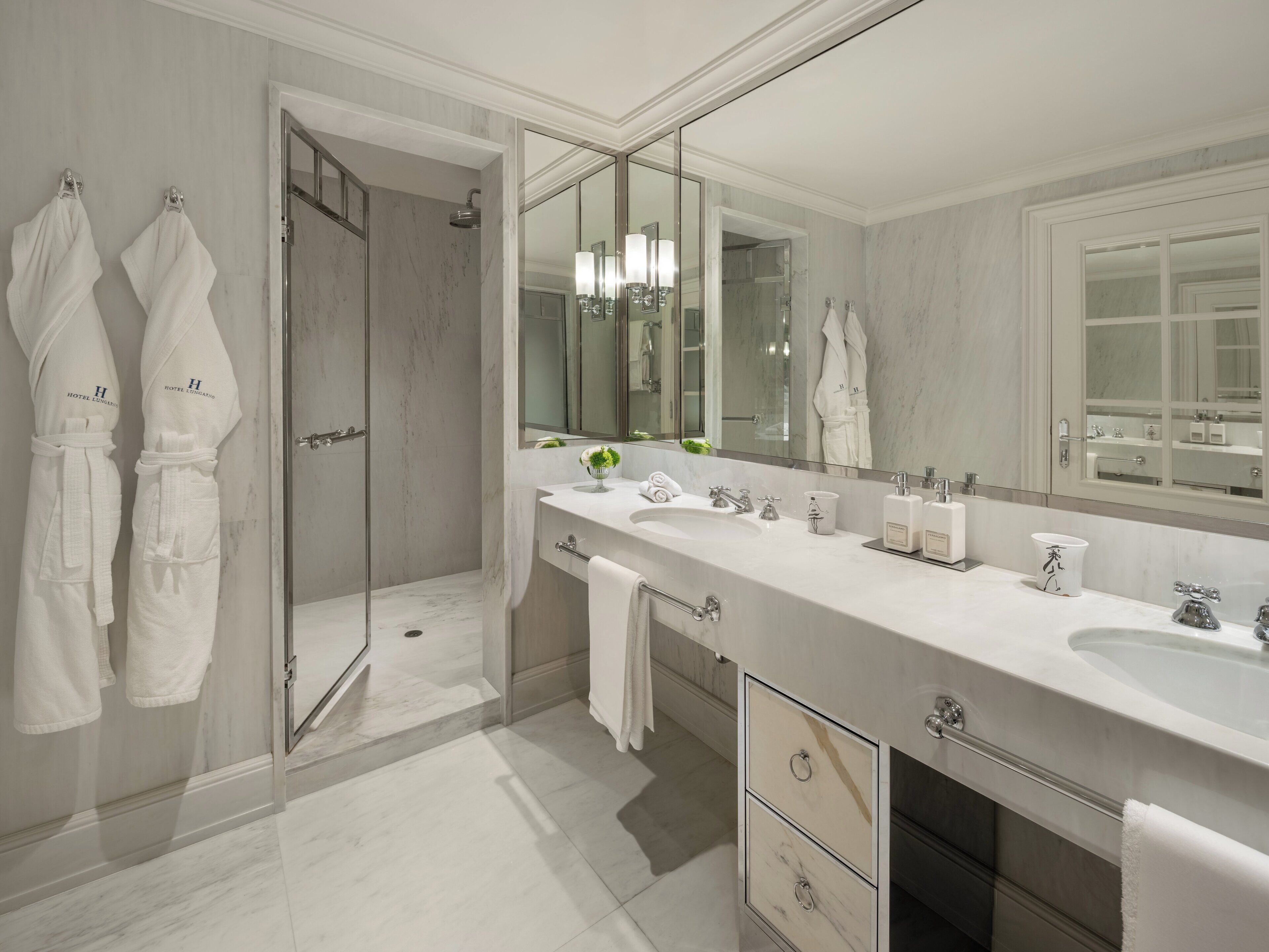 Un baño moderno con un espejo grande, dos lavamanos, una ducha y cabina de ducha con mampara de vidrio.