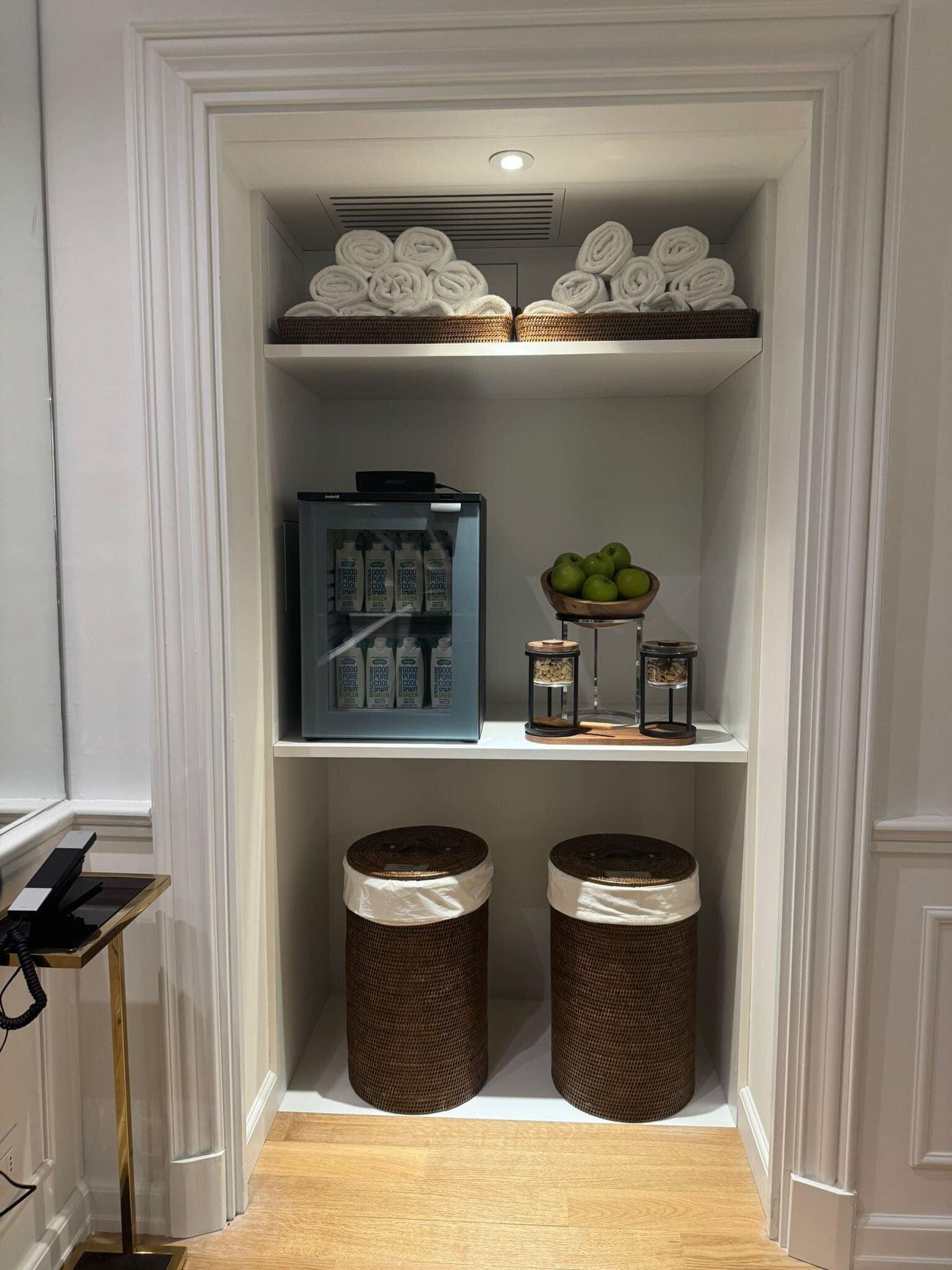 A storage closet with shelves holding rolled towels, a refrigerator, and baskets.