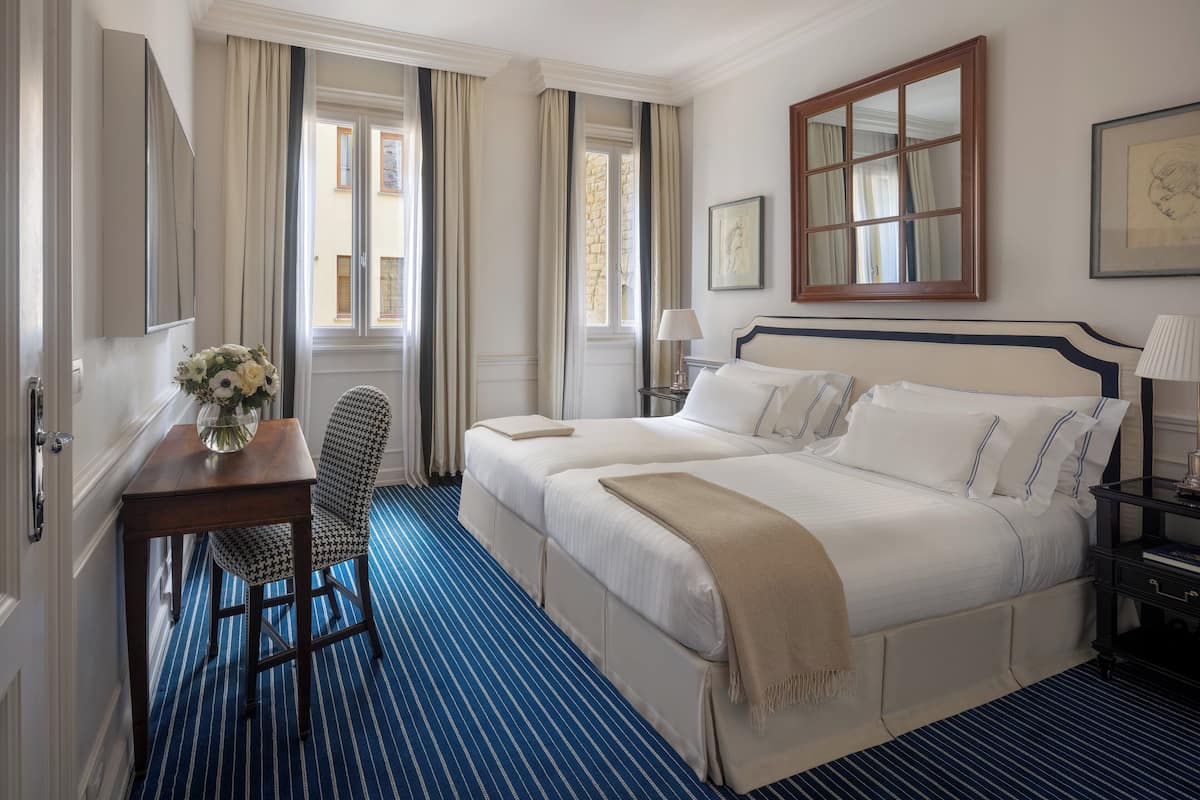 Hotellihuone, jossa on suuri sänky, työpöytä tuolilla, ikkuna verhoilla ja seinällä oleva kehystetty taulu.