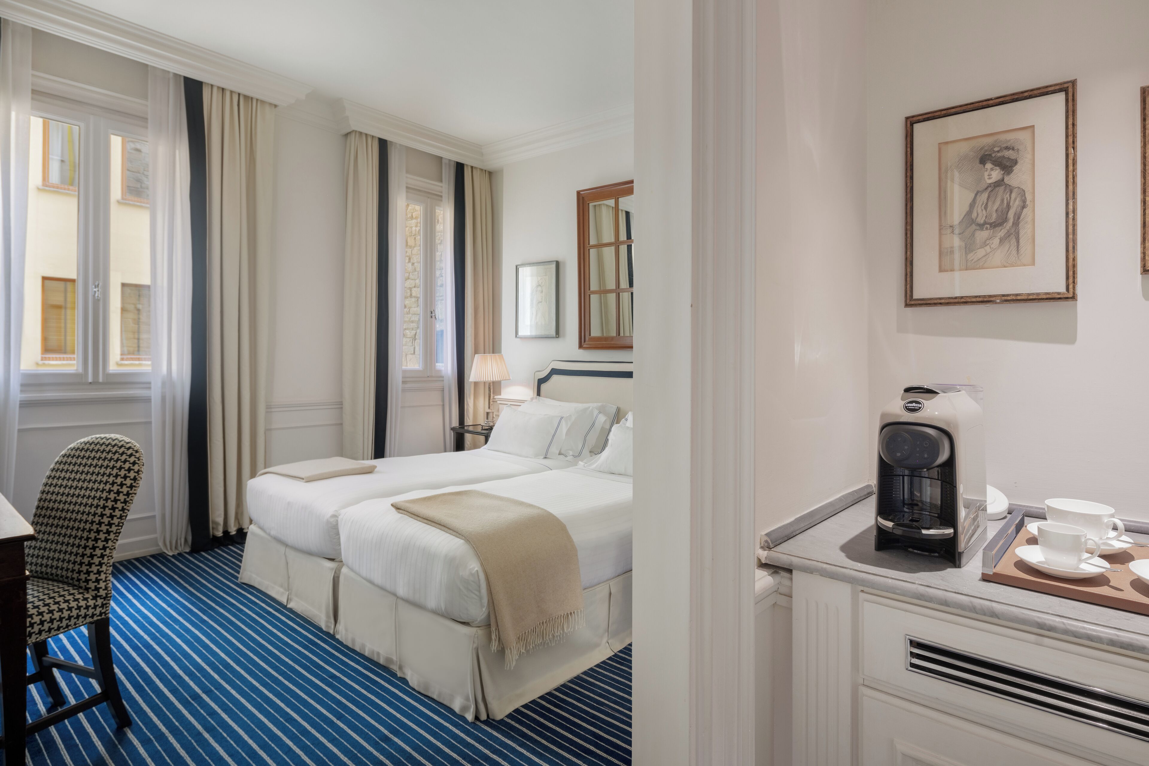 A hotel room with a bed, a chair, a coffee maker, and a framed picture on the wall.