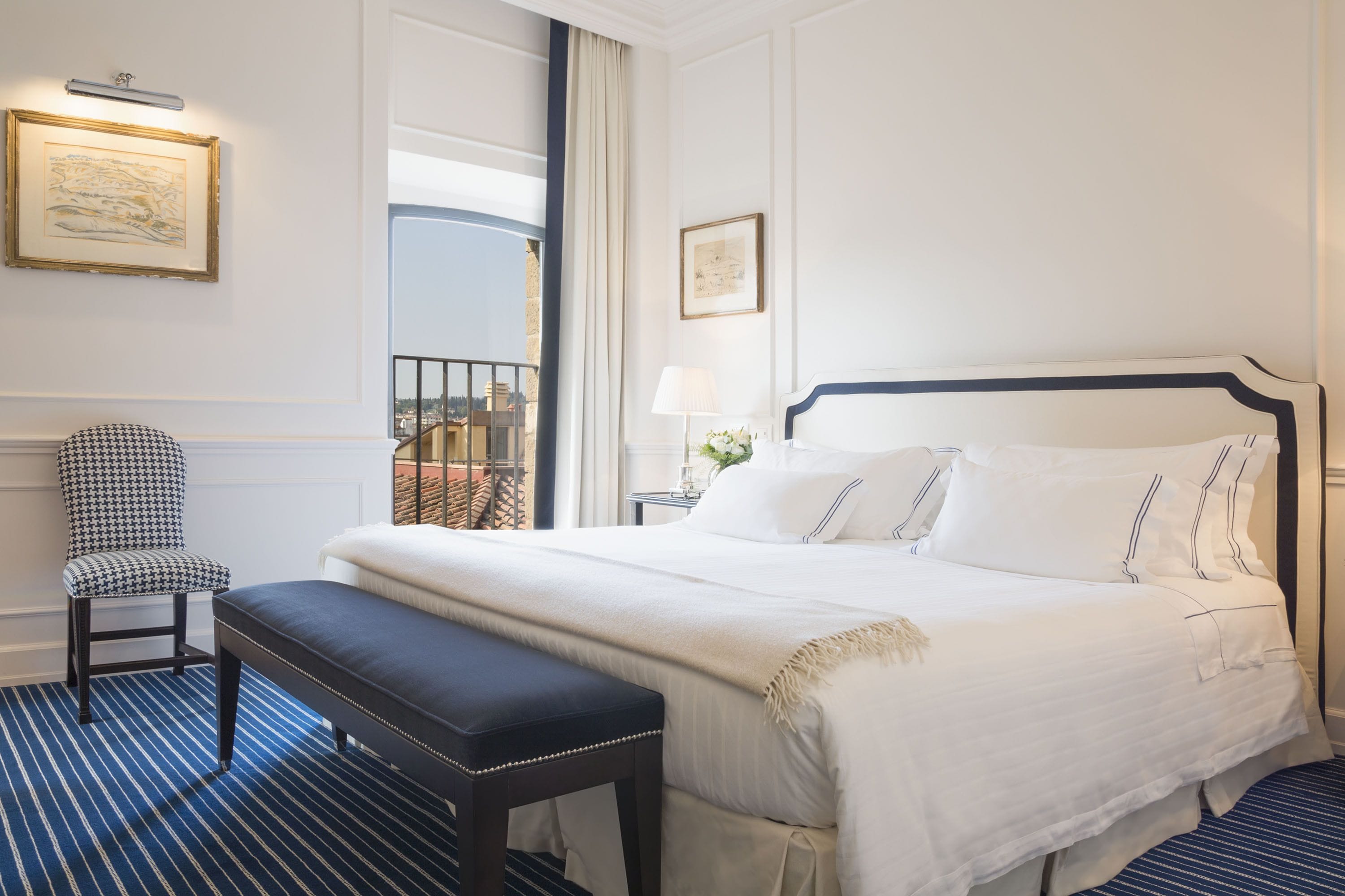A hotel room with a large bed, a bench, a chair, and a balcony with a view.