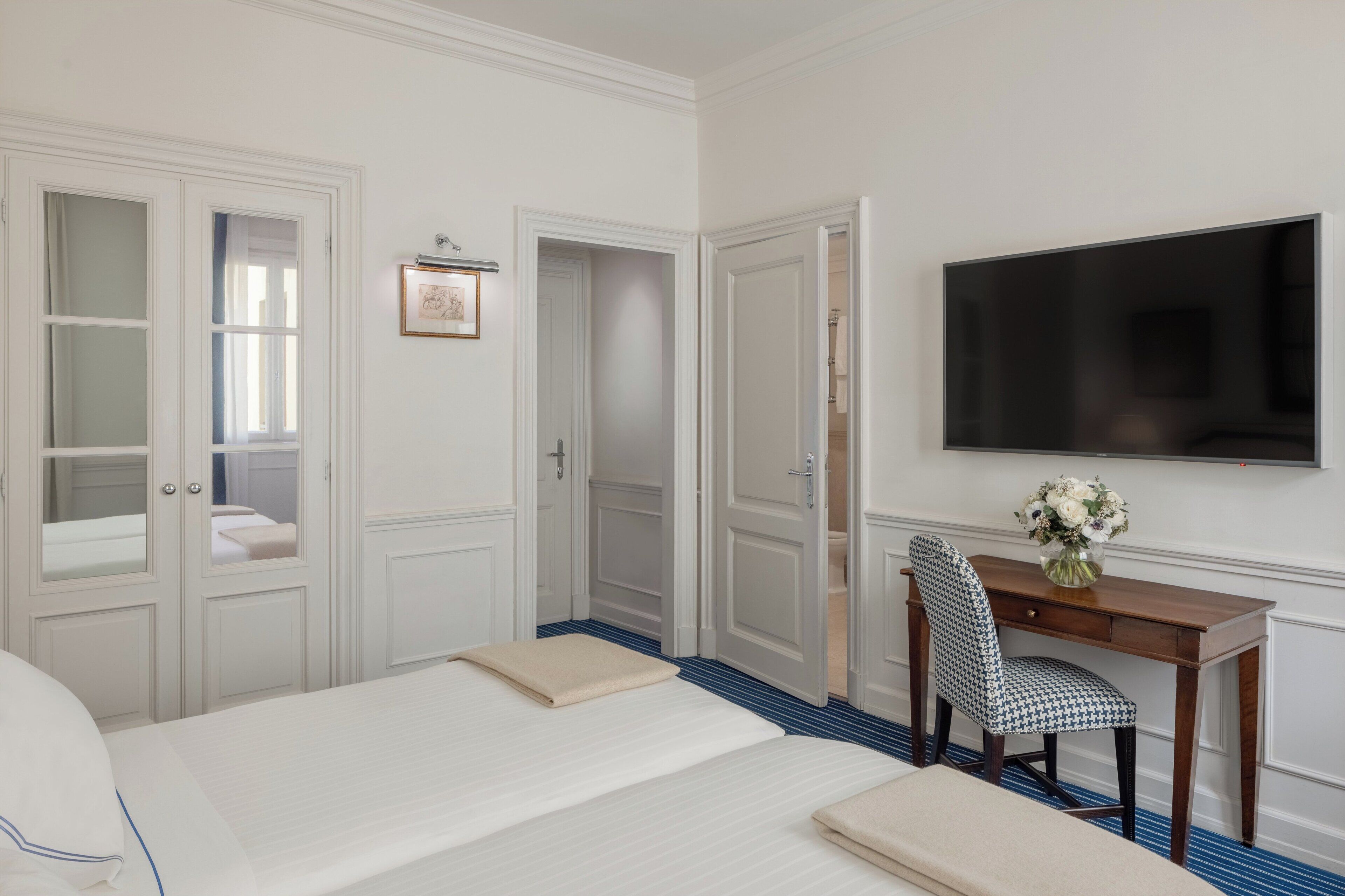 Una camera d'albergo con due letti, una scrivania con una sedia, una TV a schermo piatto e un quadro appeso al muro.