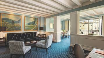 Un hall de hotel con alfombra azul, una zona de estar con sillones estampados y grandes cuadros de paisajes en la pared.
