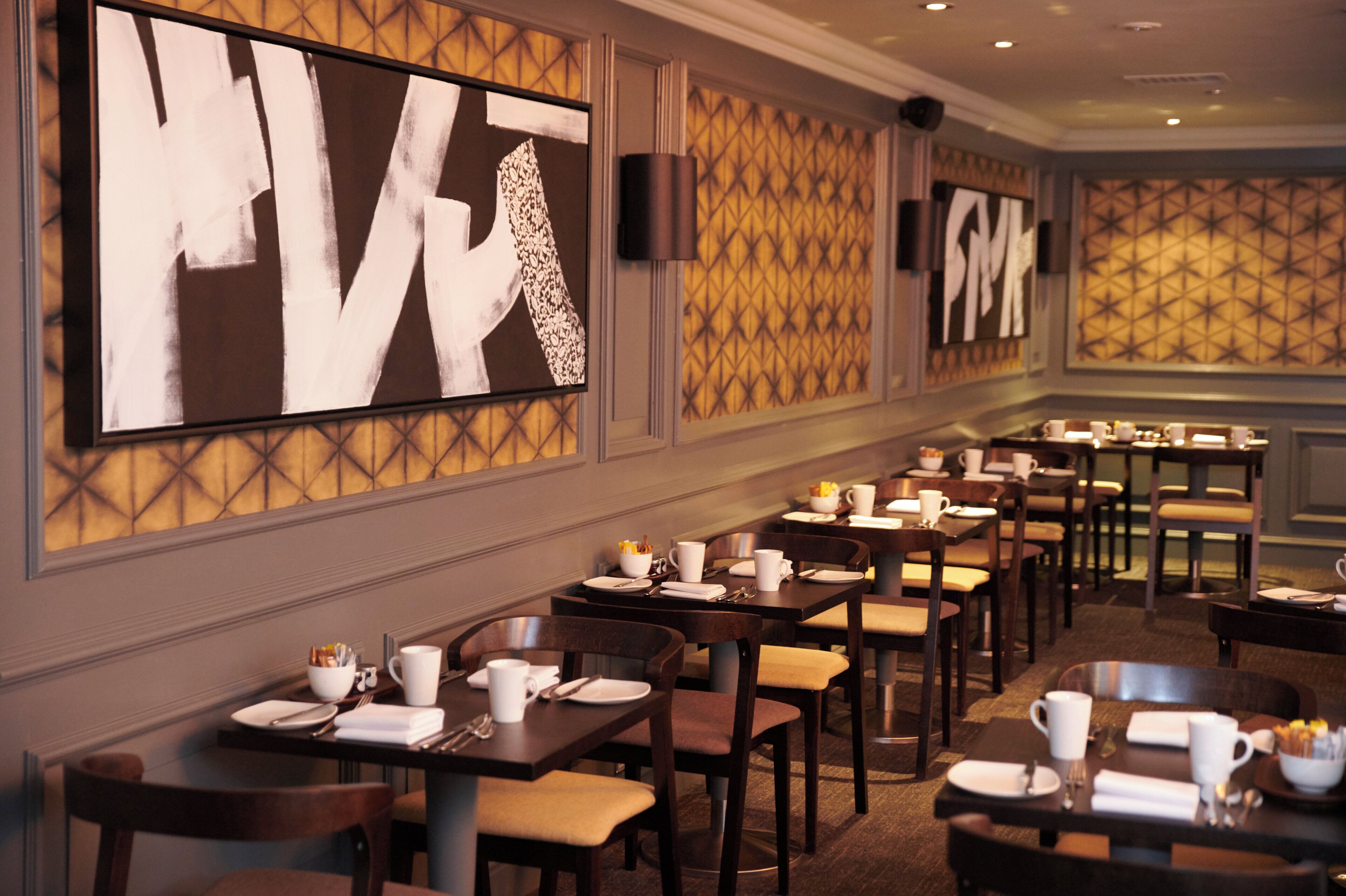 Een restaurantruimte in een hotel, ingericht voor het ontbijt met tafels, borden, bekers en bestek.