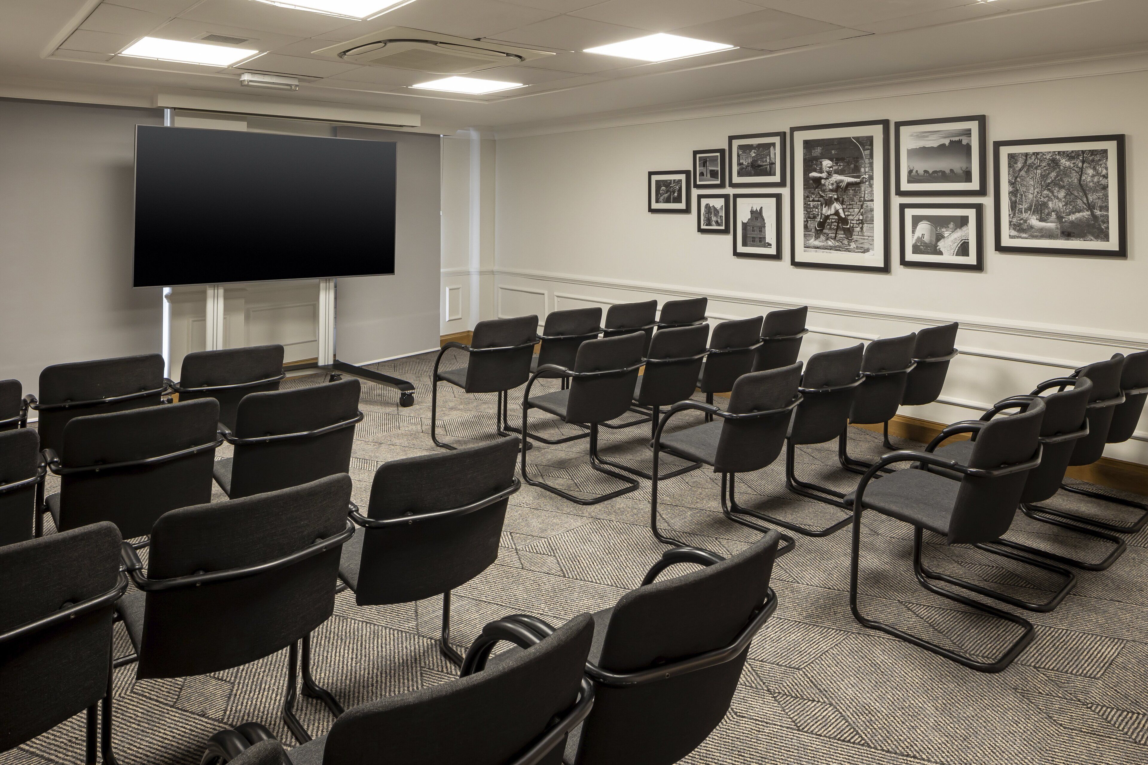 A conference room with rows of black chairs, a large flat-screen TV, and framed pictures on the wall.