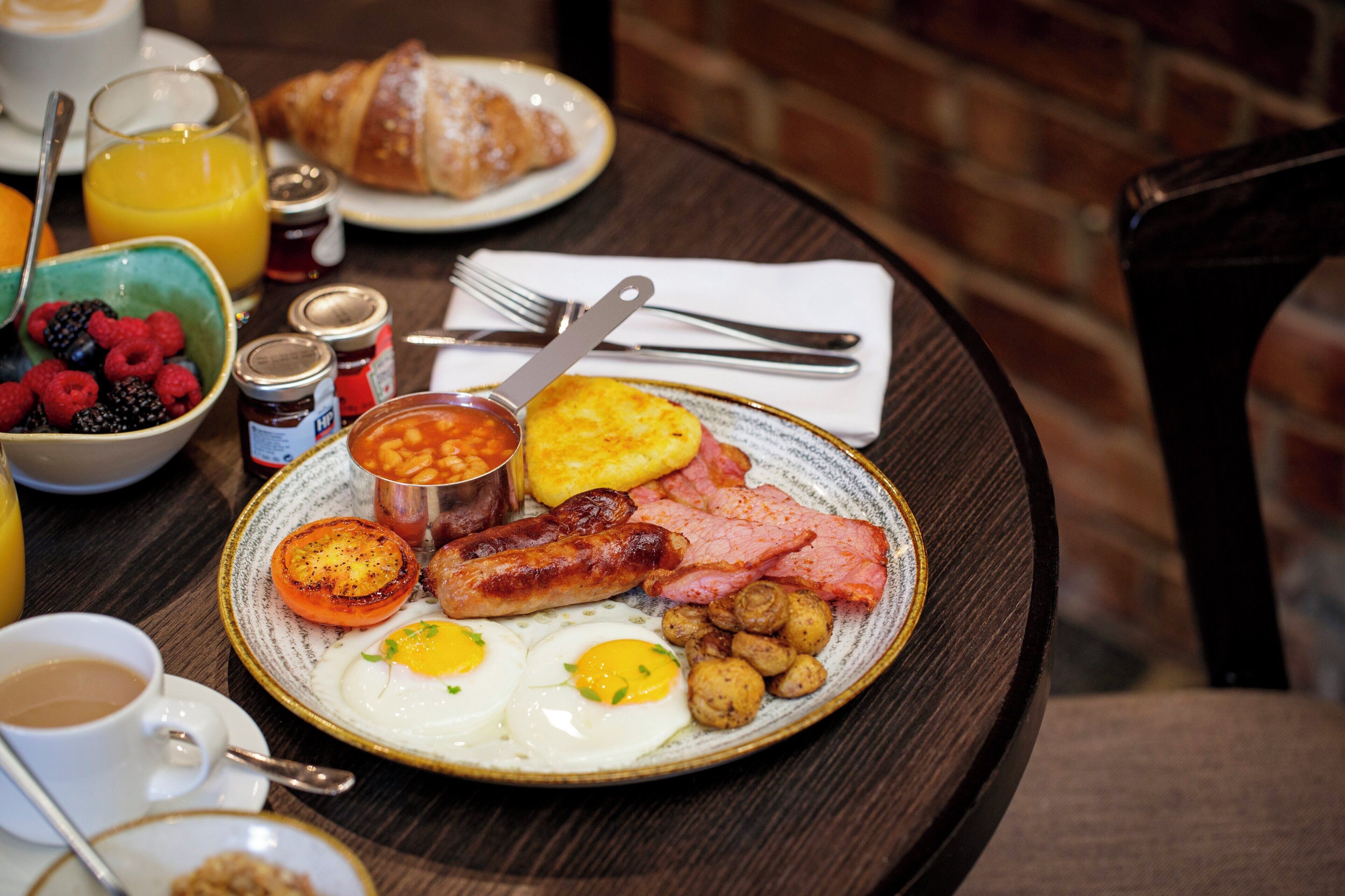 Une assiette de petit-déjeuner comprenant des œufs, des saucisses, du bacon, des toasts et un croissant.