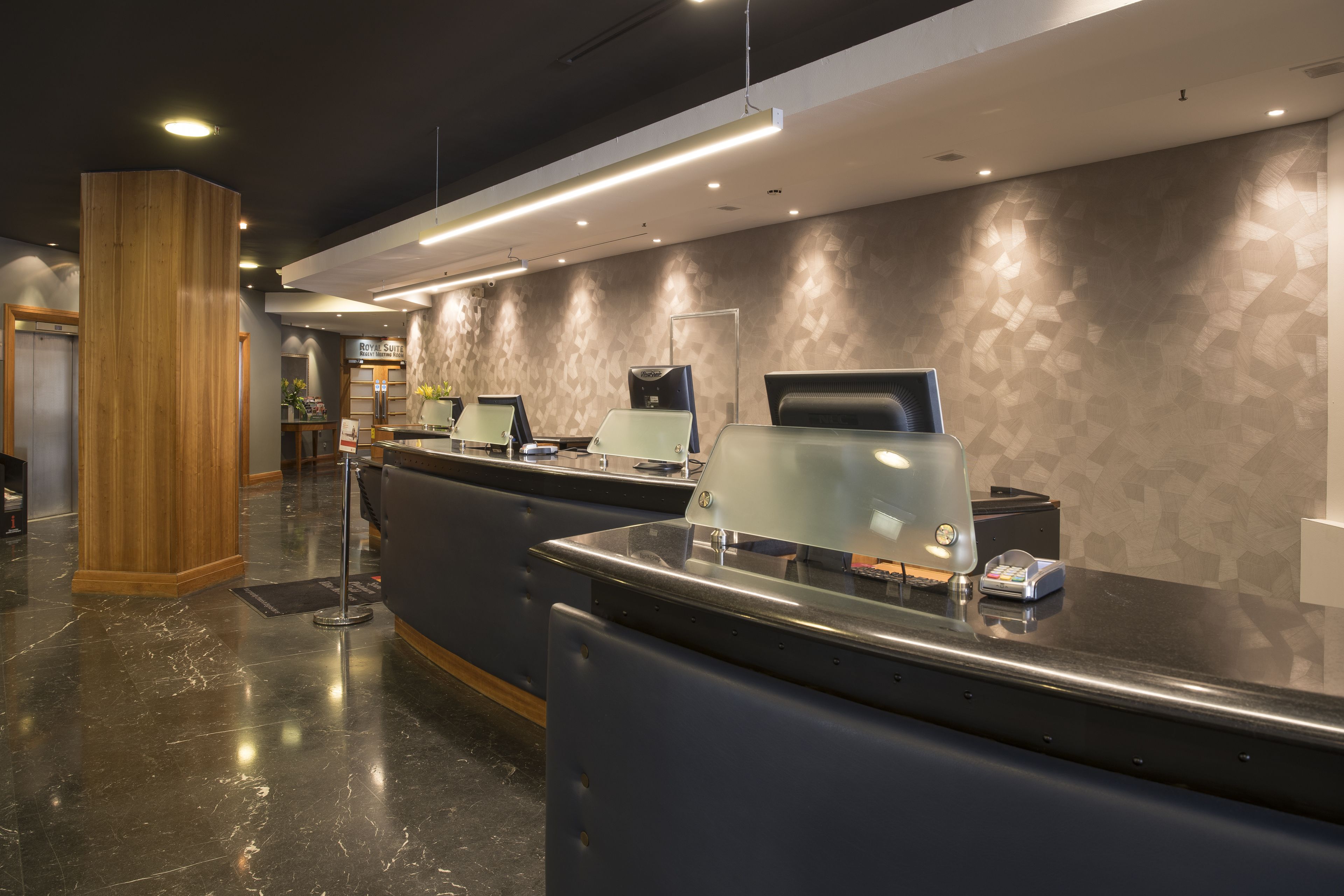 Un mostrador de recepción moderno con una pared de vidrio, un pilar de madera y una pared con diseño en el vestíbulo de un hotel.