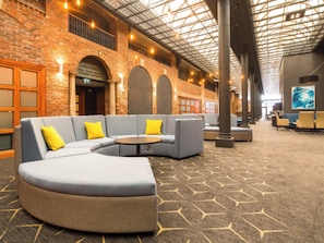 A spacious lobby with a curved seating area, a high ceiling with skylights, and a brick wall. - Crowne Plaza Nottingham by IHG (Nottingham)