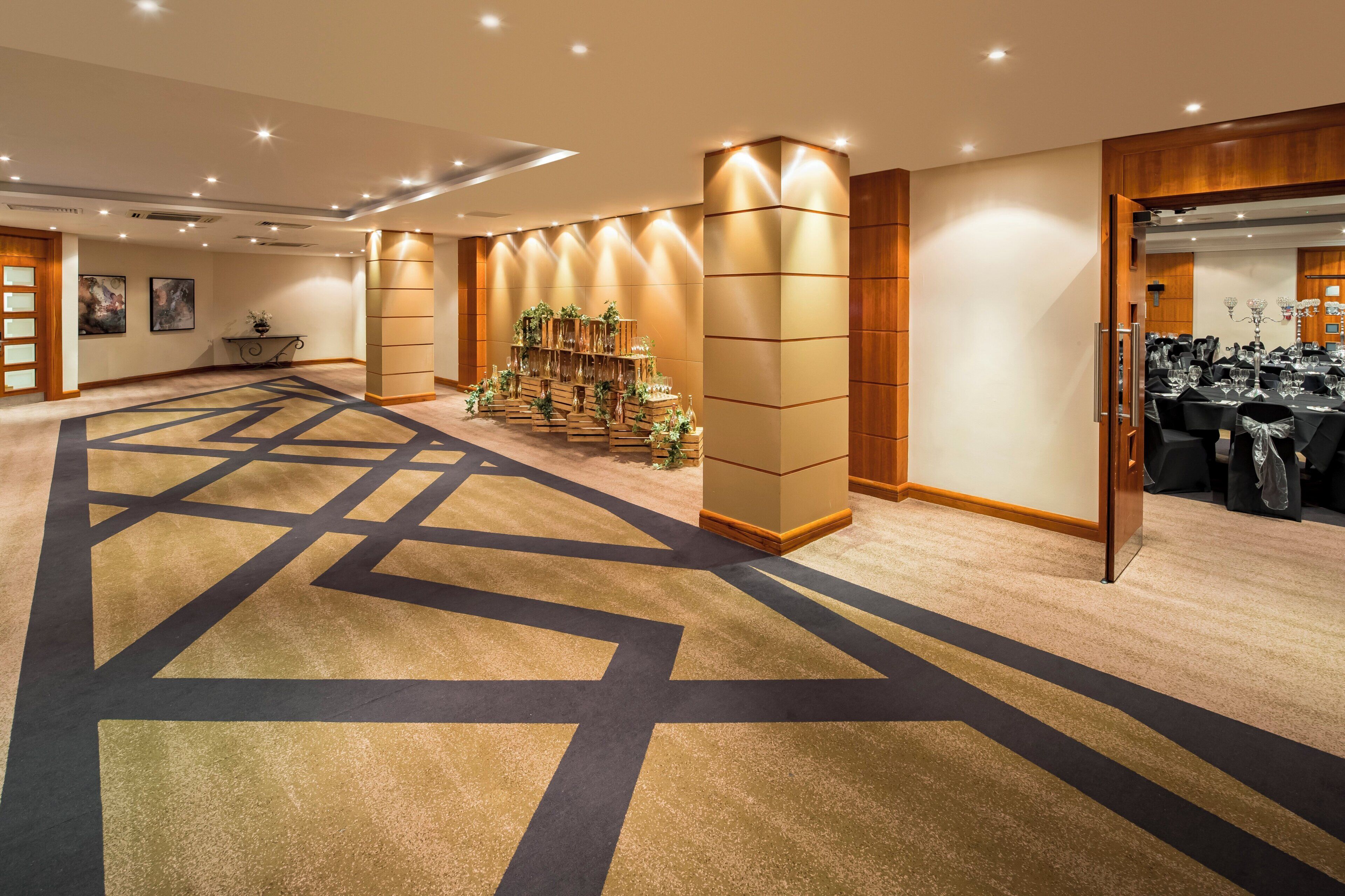 Un vestíbulo de hotel con suelo alfombrado, un mostrador de recepción y una zona de estar con mesas y sillas.