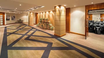 Un vestíbulo de hotel con suelo alfombrado, un mostrador de recepción y una zona de estar con mesas y sillas.