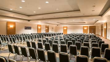 Un salón de conferencias con filas de sillas, un panel de pared de madera y luces empotradas en el techo.