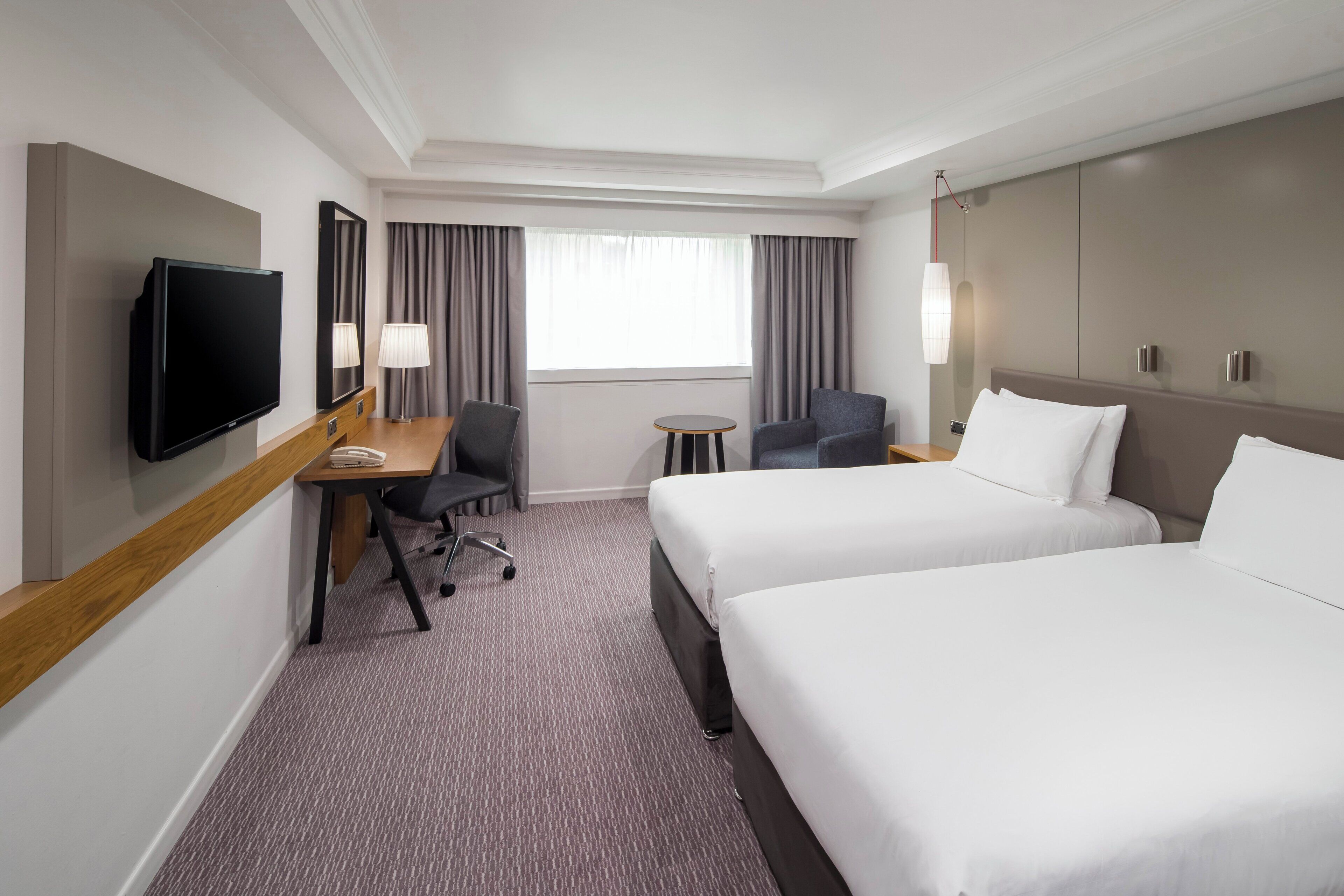 A hotel room with two beds, a desk with a chair, a television, and a small table.