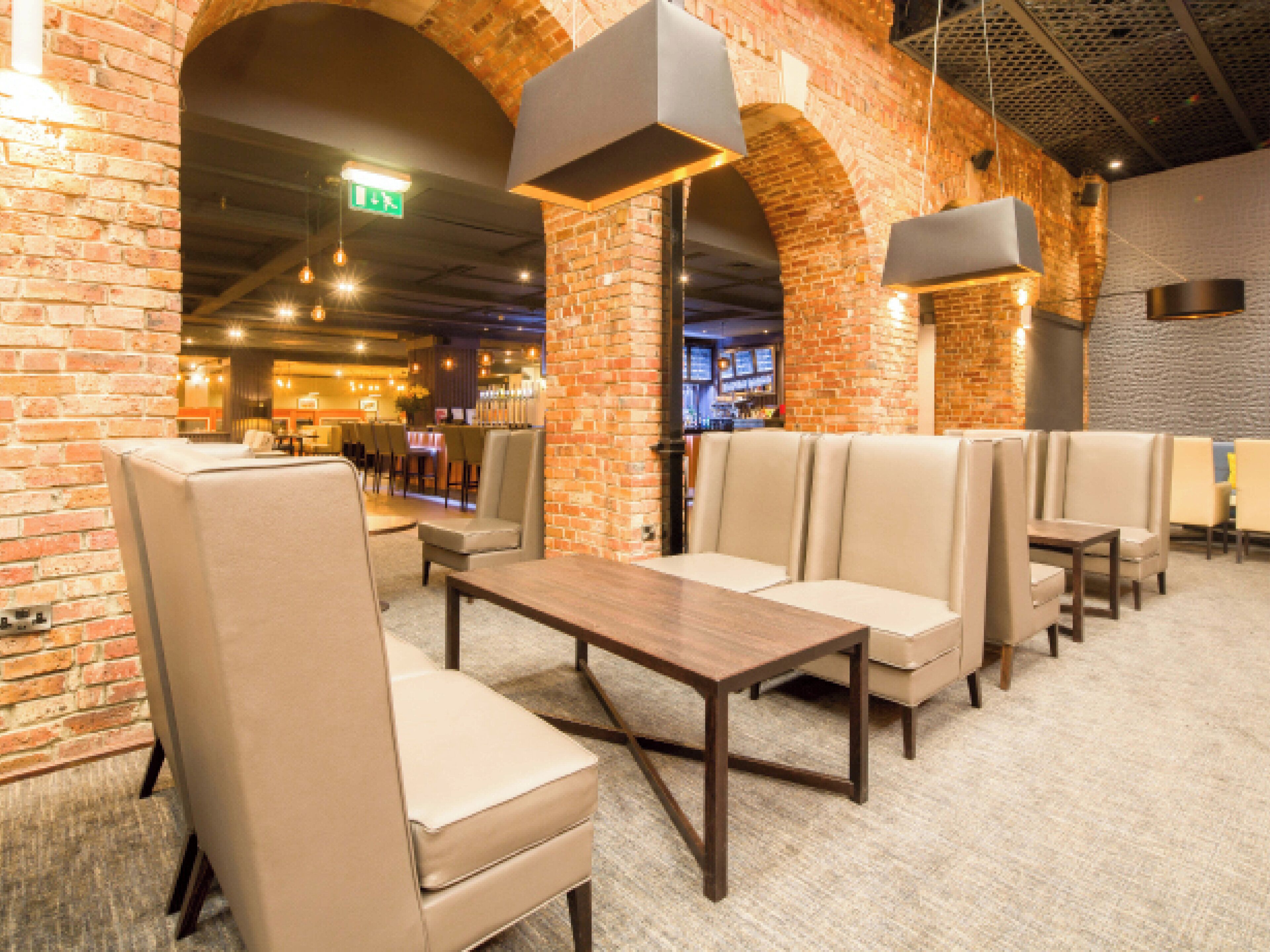 A restaurant interior with brick walls, cushioned booths, and hanging pendant lights.