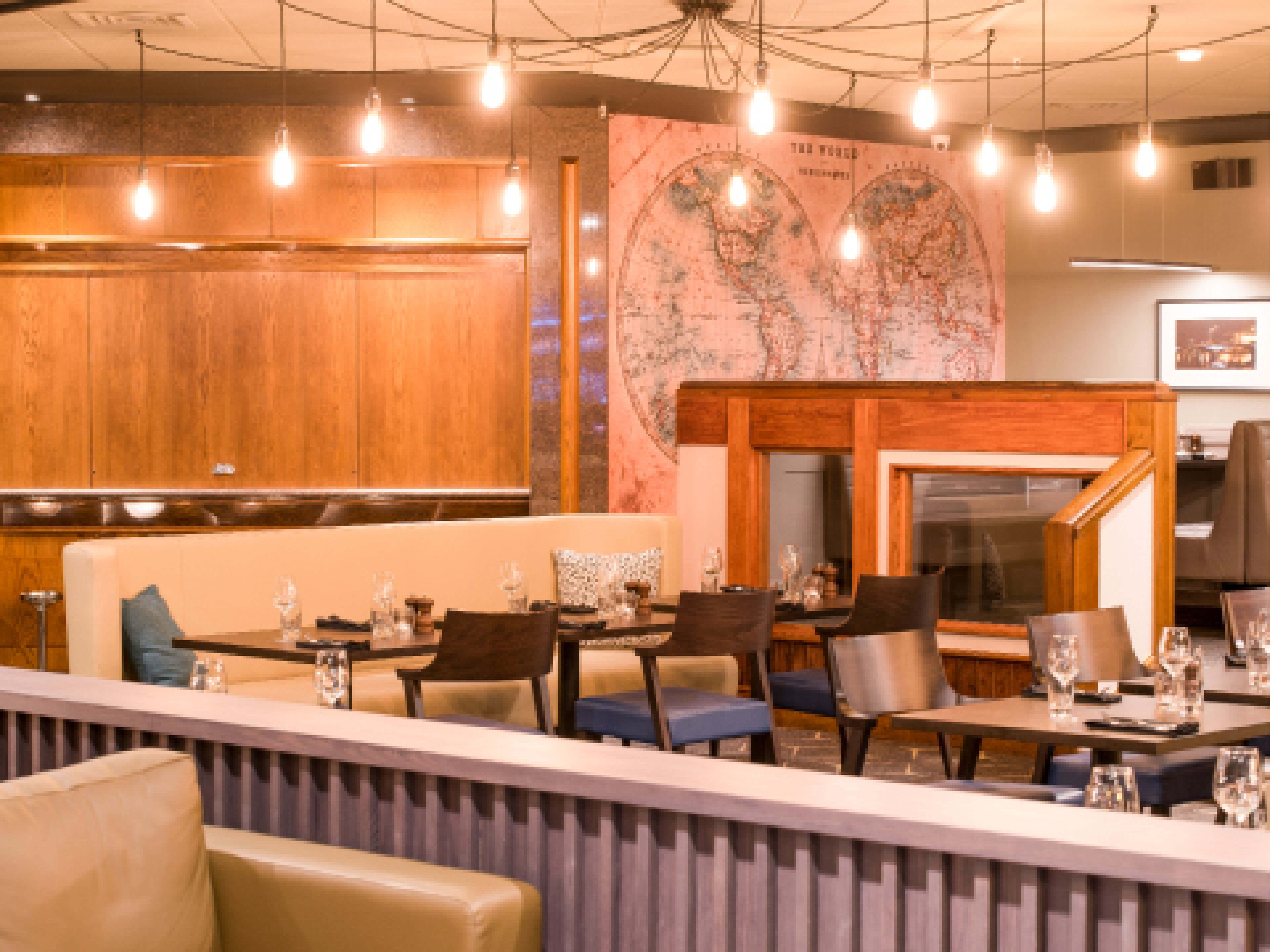 Un restaurant avec des boiseries, une fresque représentant une carte du monde et des ampoules suspendues.