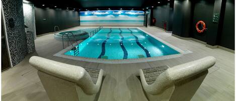 A swimming pool with a view of the beach, lounge chairs, and a lifebuoy on the wall.