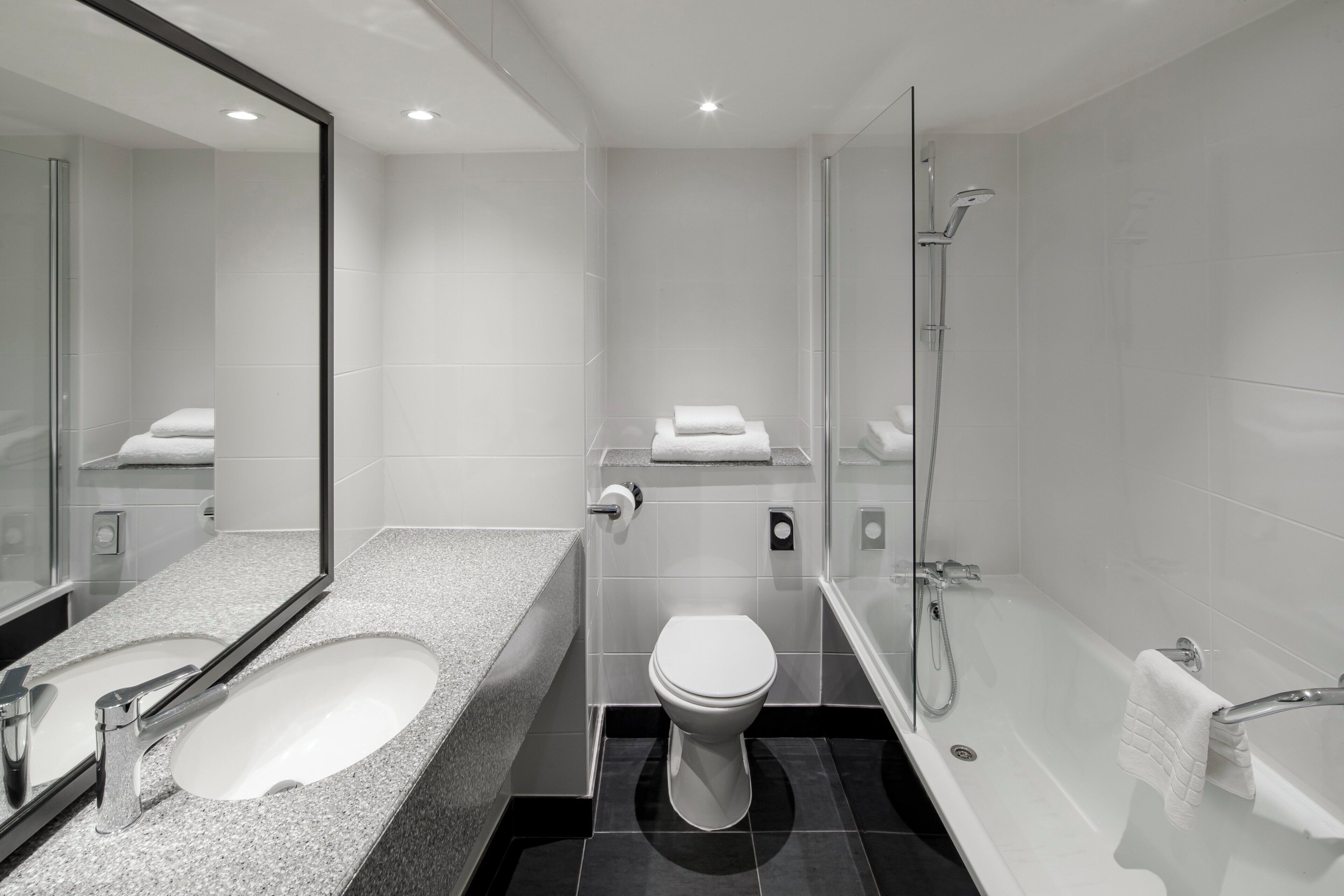 A modern bathroom with a granite countertop sink, a toilet, and a glass-enclosed shower area.