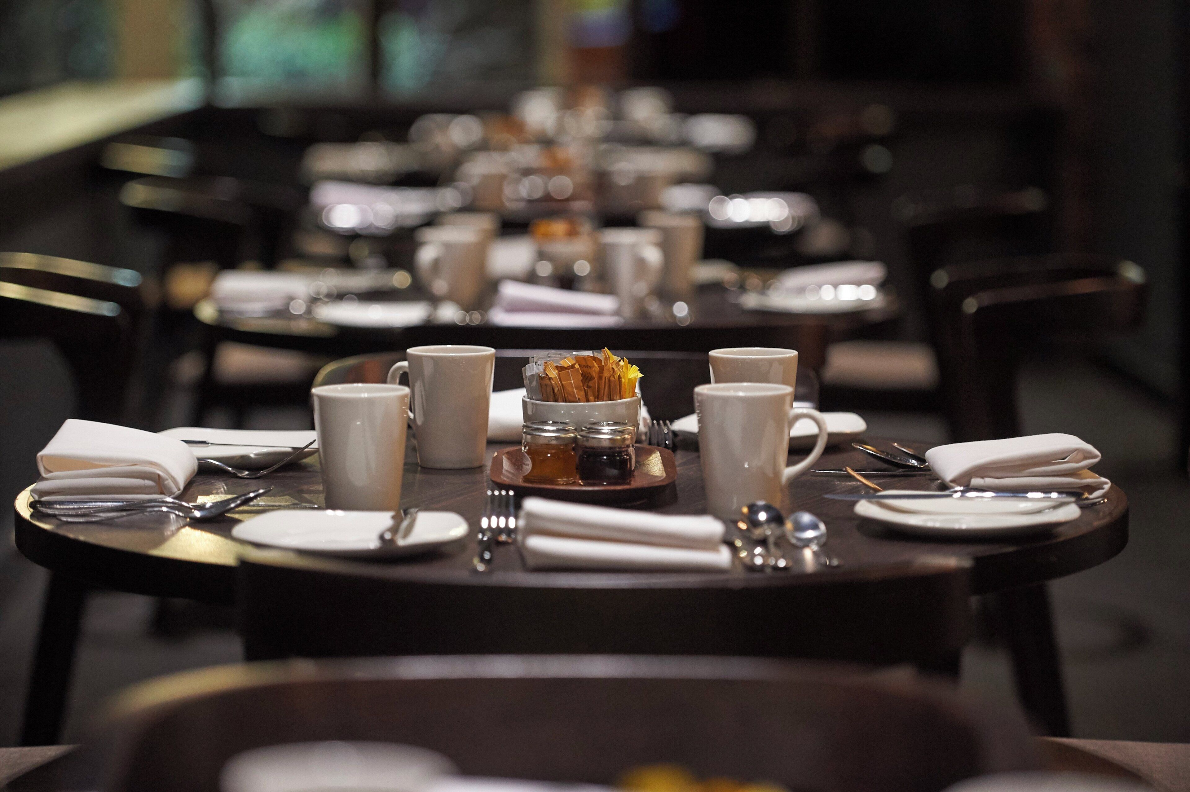A restaurant table set with white plates, cups, and cutlery.