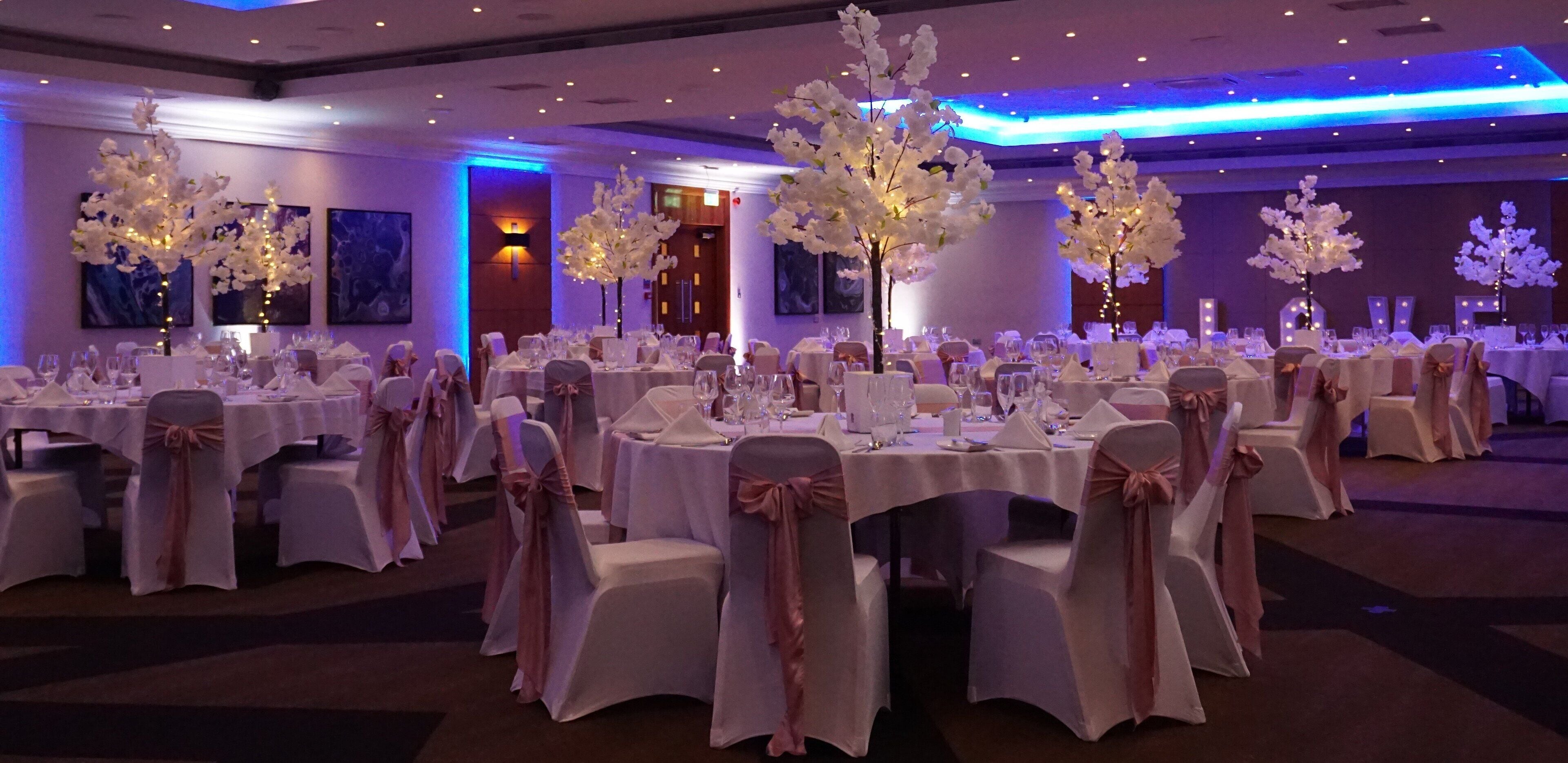 A banquet hall with round tables, white tablecloths, and chairs with pink sashes.