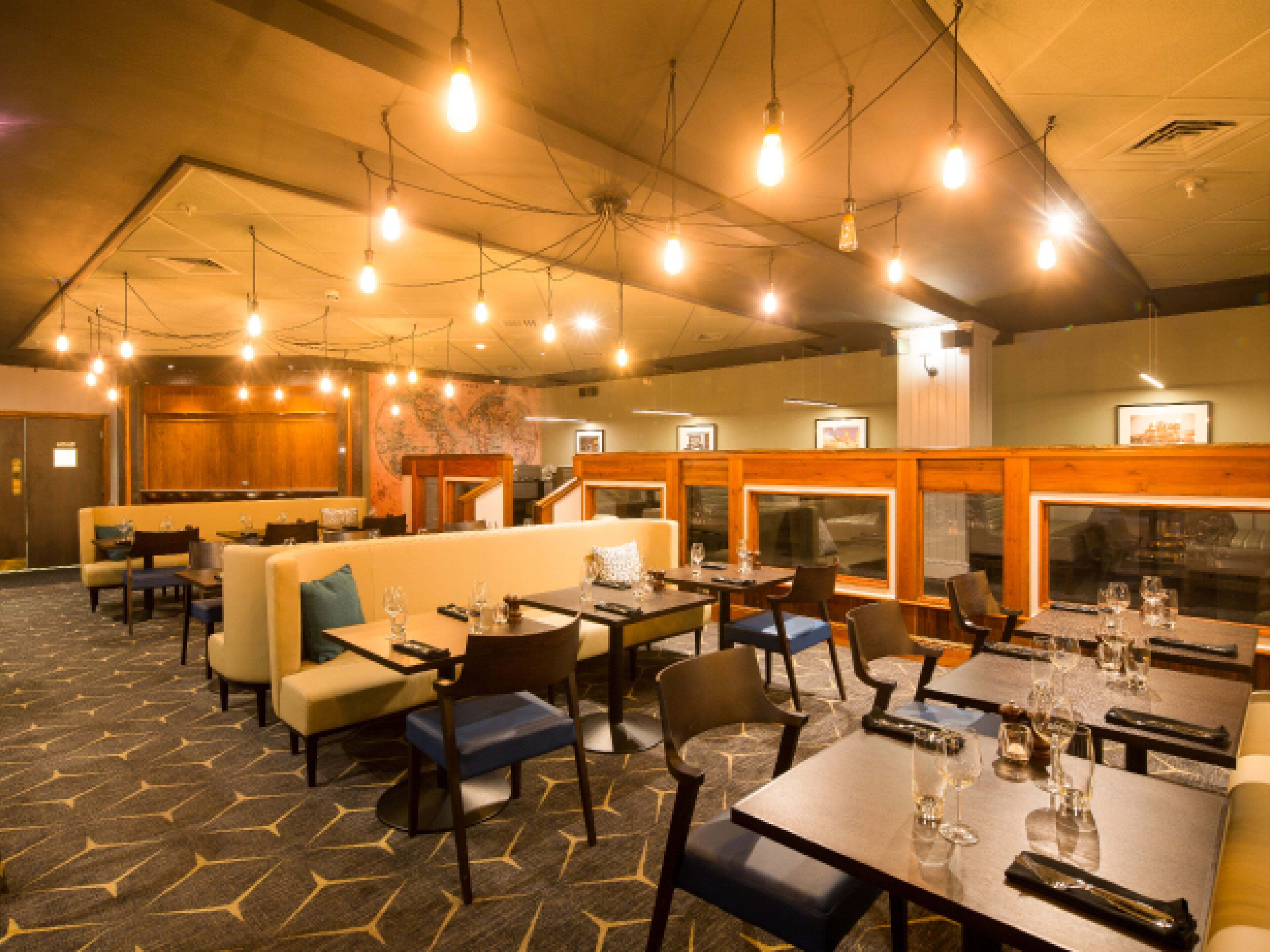A restaurant with multiple seating options including booths and tables, overhead lighting, and a patterned carpet.