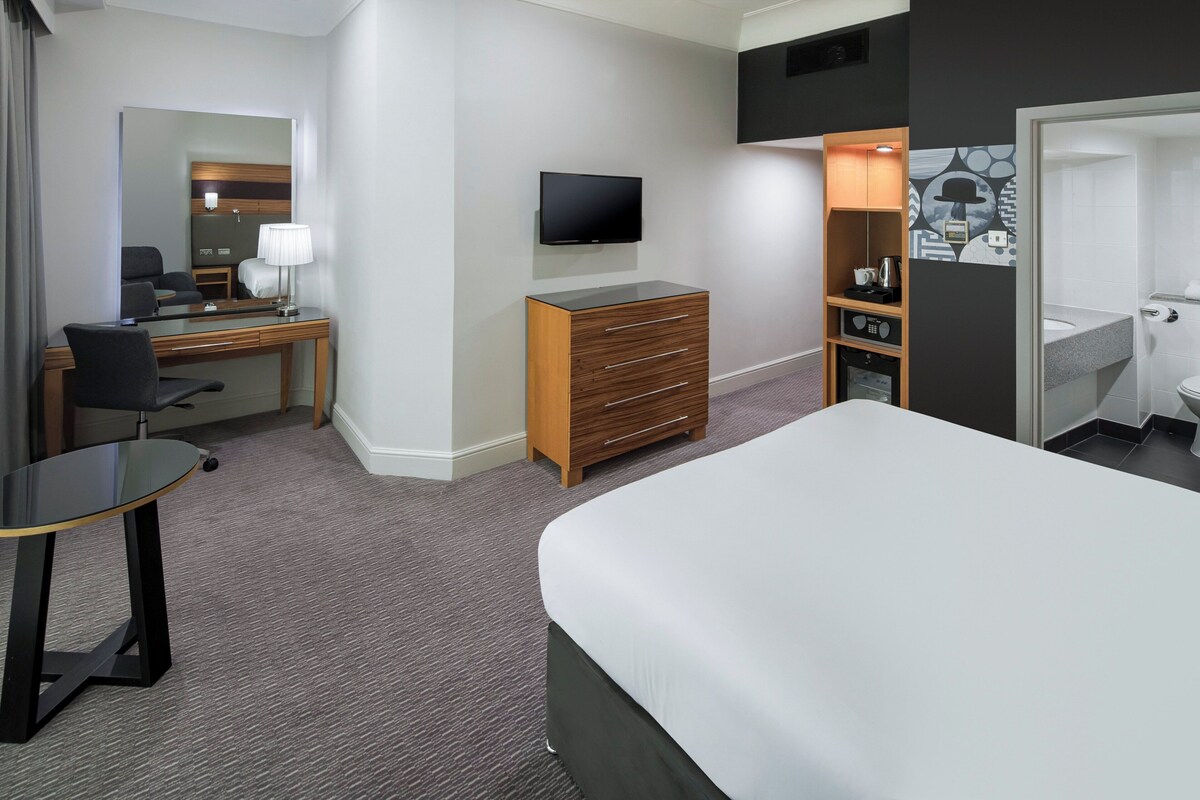 Ein Hotelzimmer mit einem Bett, einem Schreibtisch mit Stuhl, einem Fernseher, einem Kleiderschrank und einem Badezimmer.