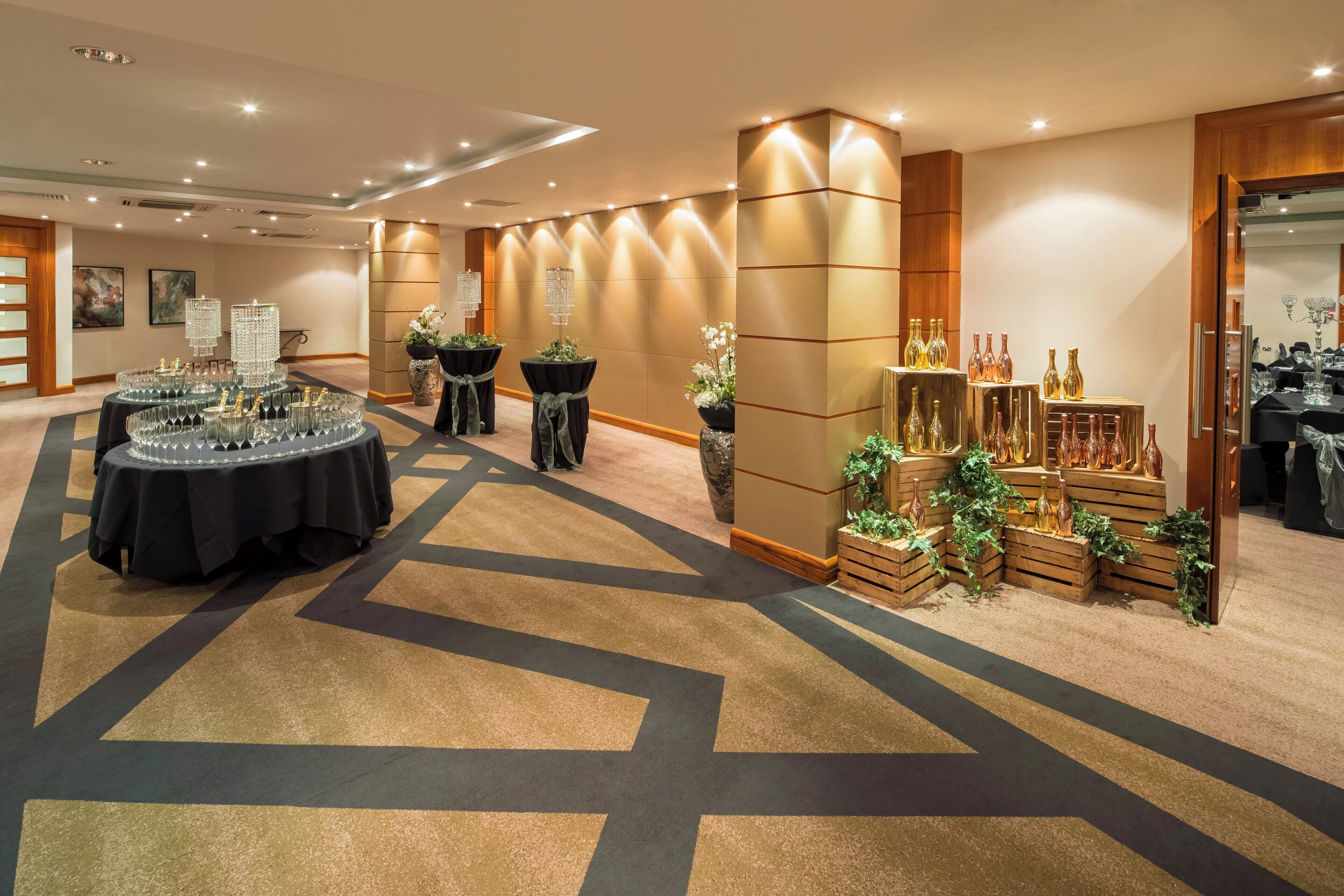 A hotel lobby with a reception desk, a seating area with tables, and a display of bottles.