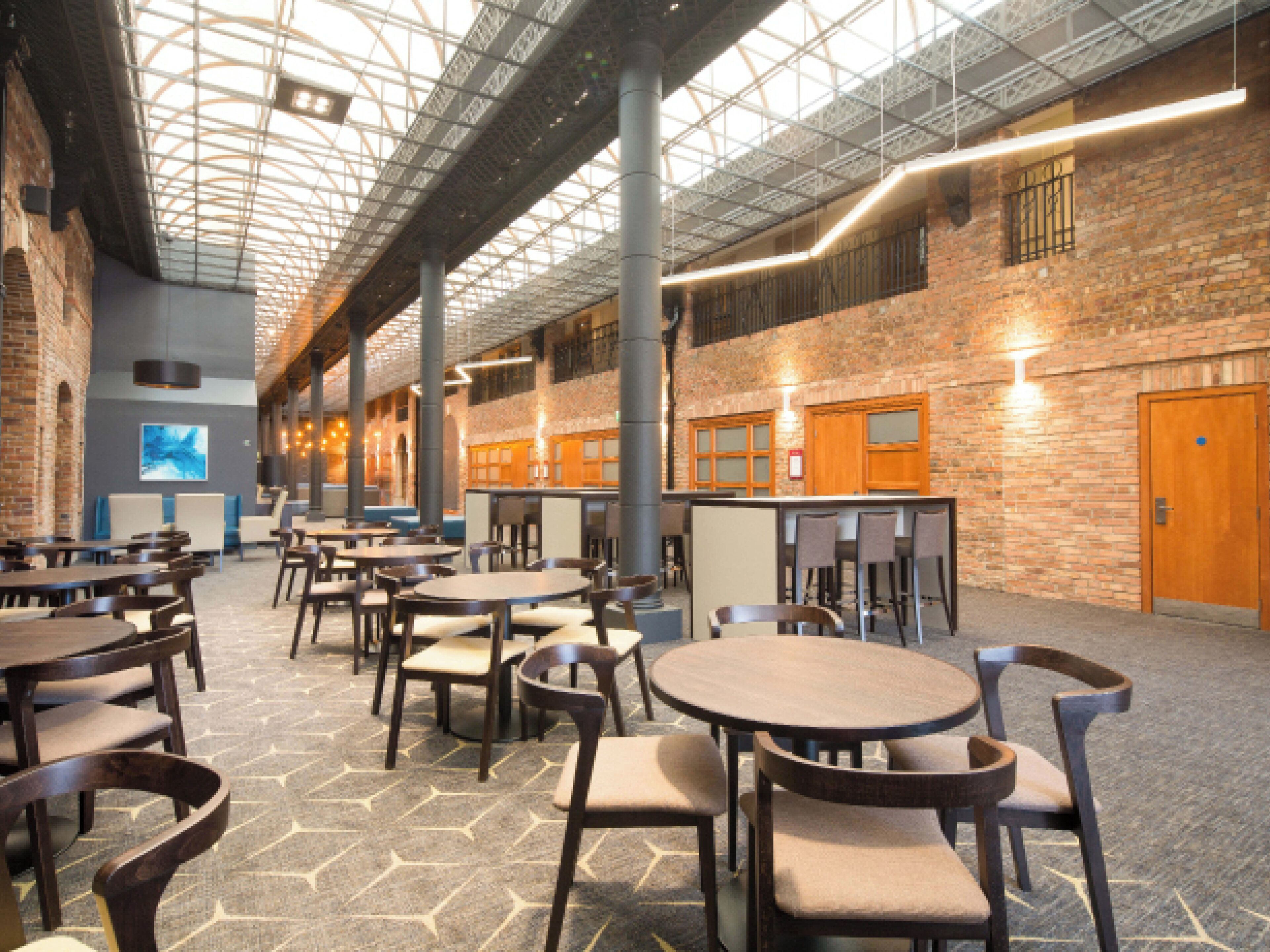 A spacious indoor area with multiple tables and chairs, a high ceiling with a skylight, and brick walls.