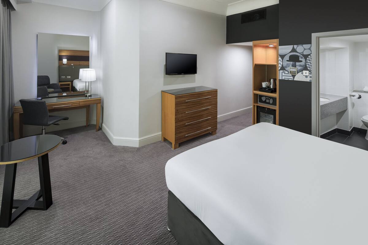 A hotel room with a bed, a desk with a chair, a dresser, a television, and a bathroom.