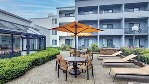 A courtyard with outdoor seating, including round tables and chairs, and a covered seating area with a glass roof. - Courtyard by Marriott Chicago Glenview/Northbrook (Northbrook)