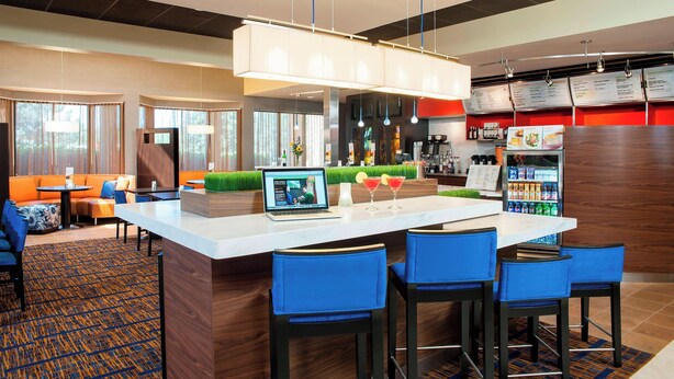 A hotel lobby with a reception desk, bar area, seating with blue chairs, and a large island with bar stools. - Courtyard by Marriott Chicago Glenview/Northbrook (Northbrook)