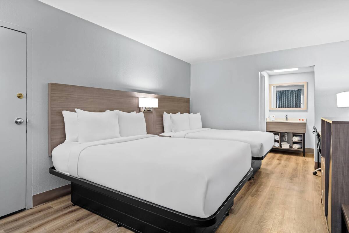 Ein Hotelzimmer mit zwei Betten, einem Nachttisch, einem Spiegel und einem kleinen Badebereich.