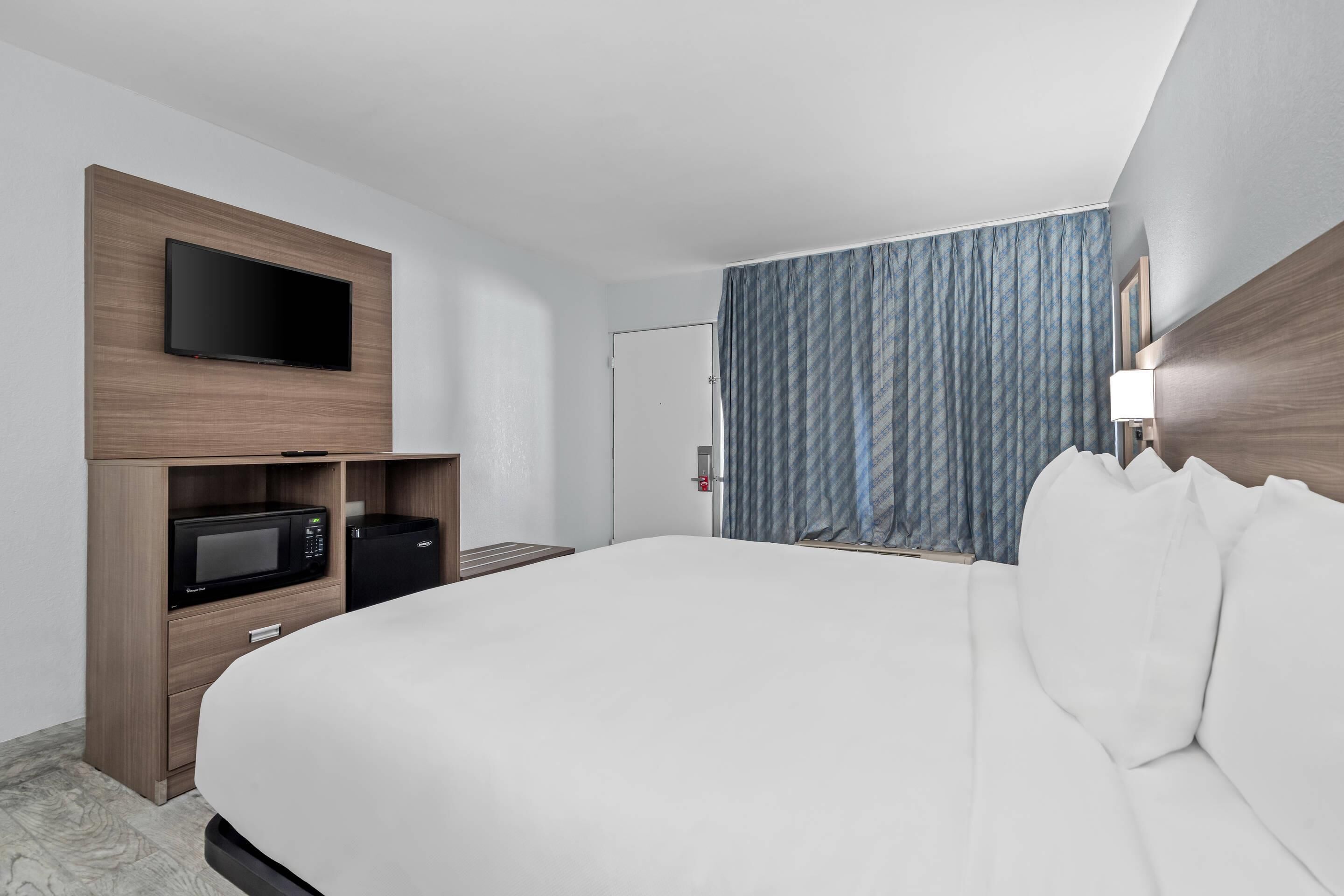 A hotel room with a large bed, a flat-screen TV mounted on a wooden panel, a microwave, and a refrigerator.