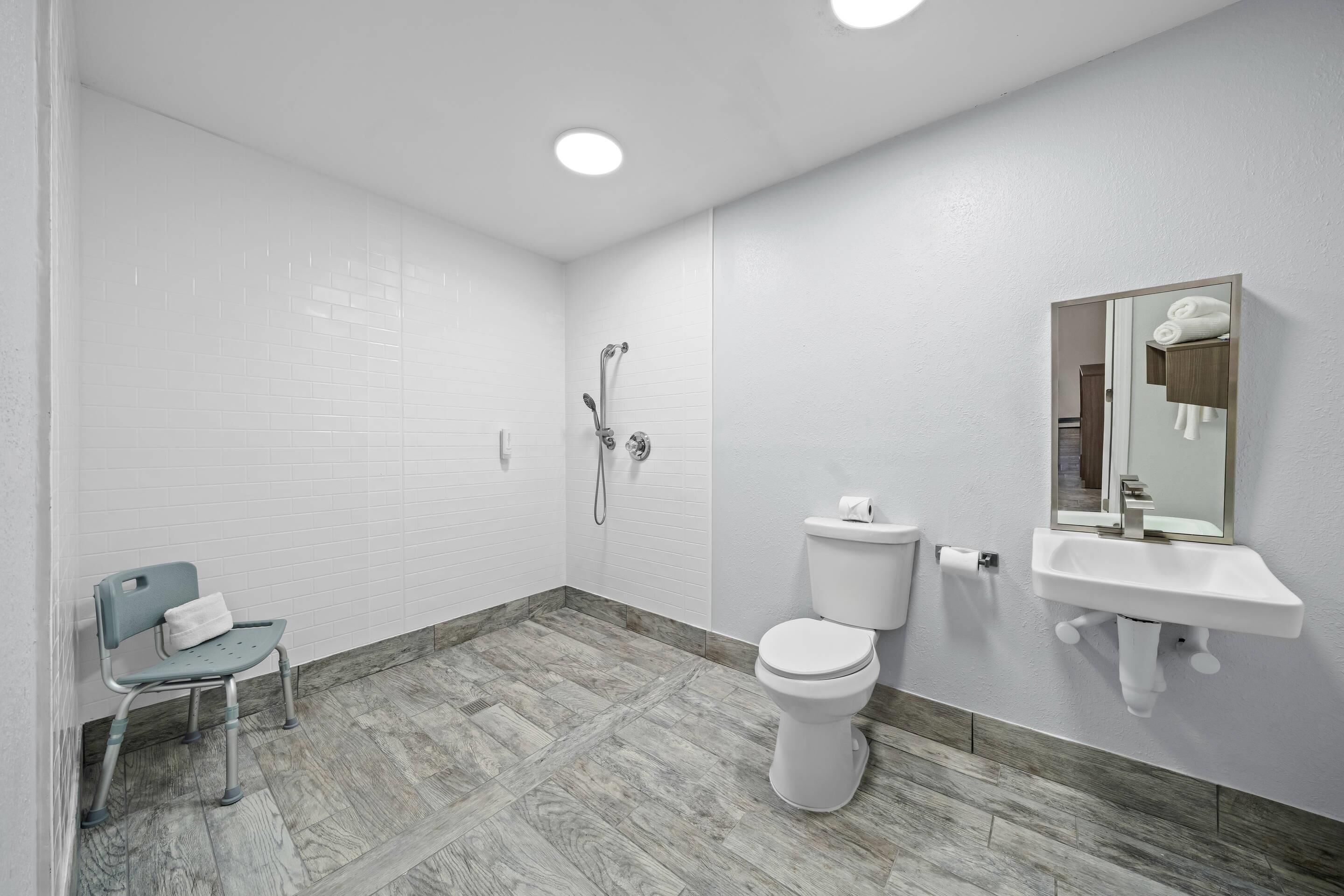 A bathroom with a toilet, sink, shower, and a chair.