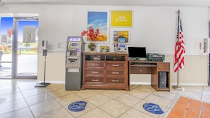 A reception area with an ATM, a wooden desk, a computer, and an American flag. - Econo Lodge Daytona Beach - Speedway (Daytona Beach)