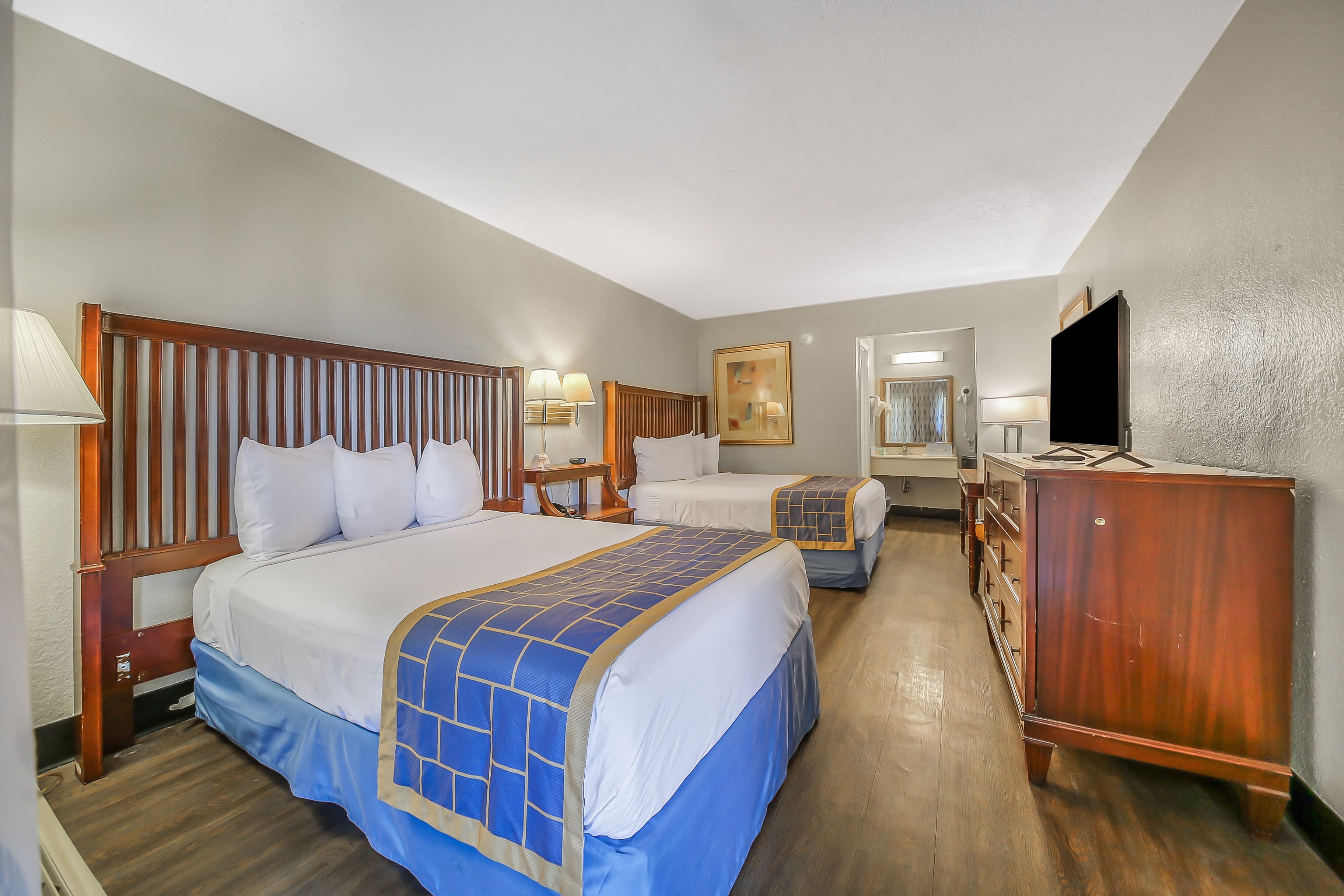 A hotel room with two beds, wooden headboards, a dresser, a television, and a mirror.