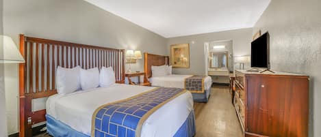 A hotel room with two beds, wooden headboards, a dresser, a television, and a mirror.